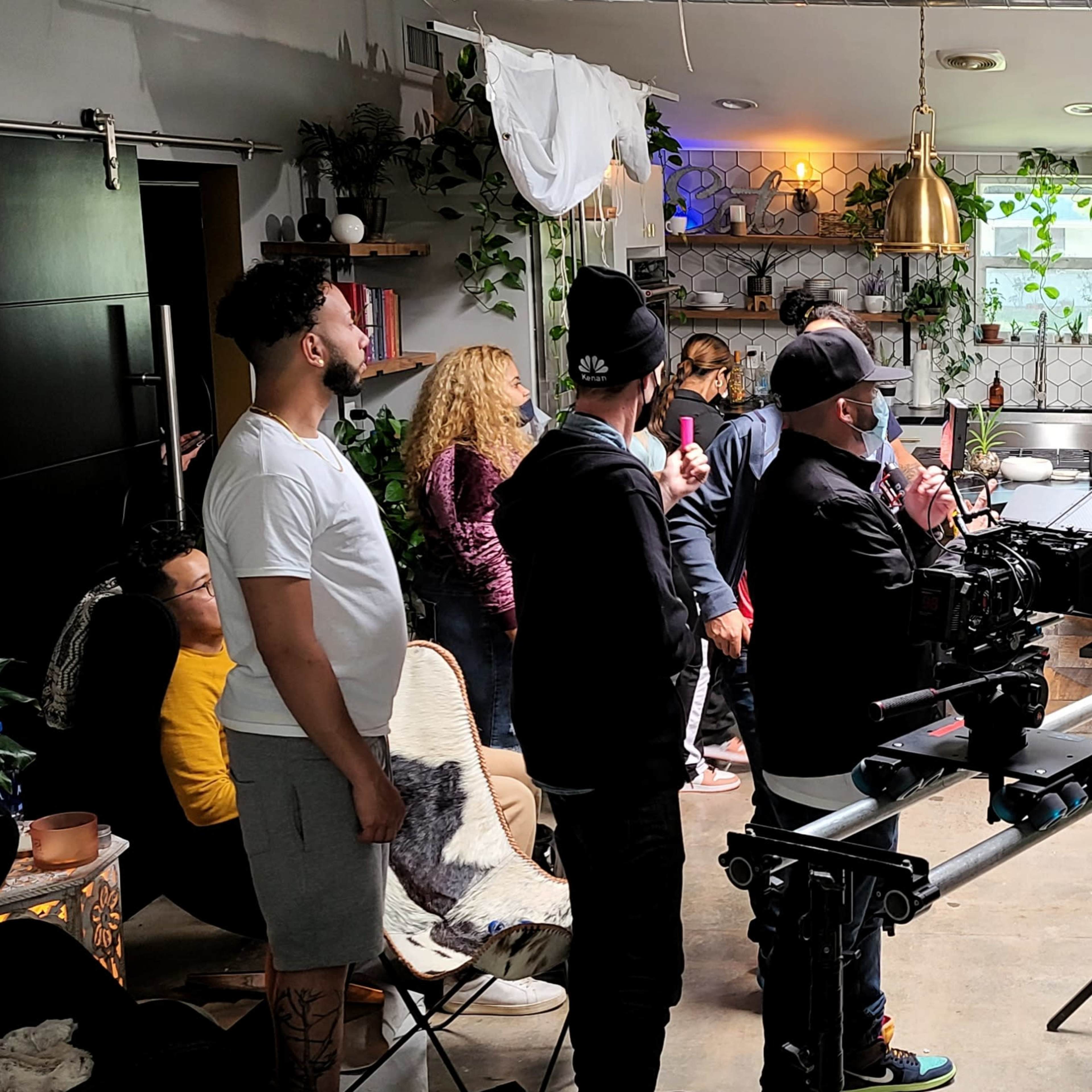 A film crew is setting up equipment in a decorated indoor space while several people observe and engage in conversation.