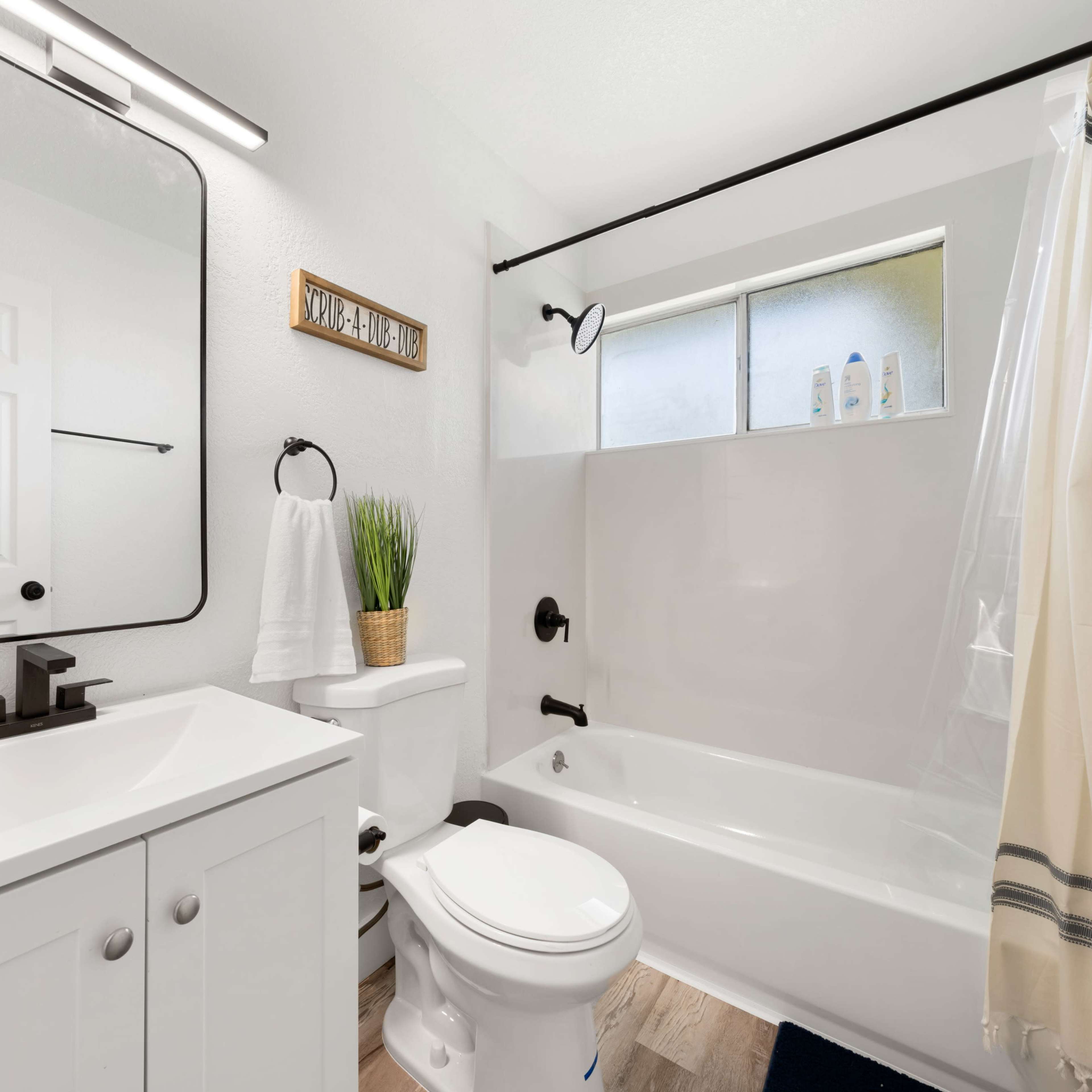 A modern bathroom with a white bathtub, a sink with a mirror, and a light-colored shower curtain.