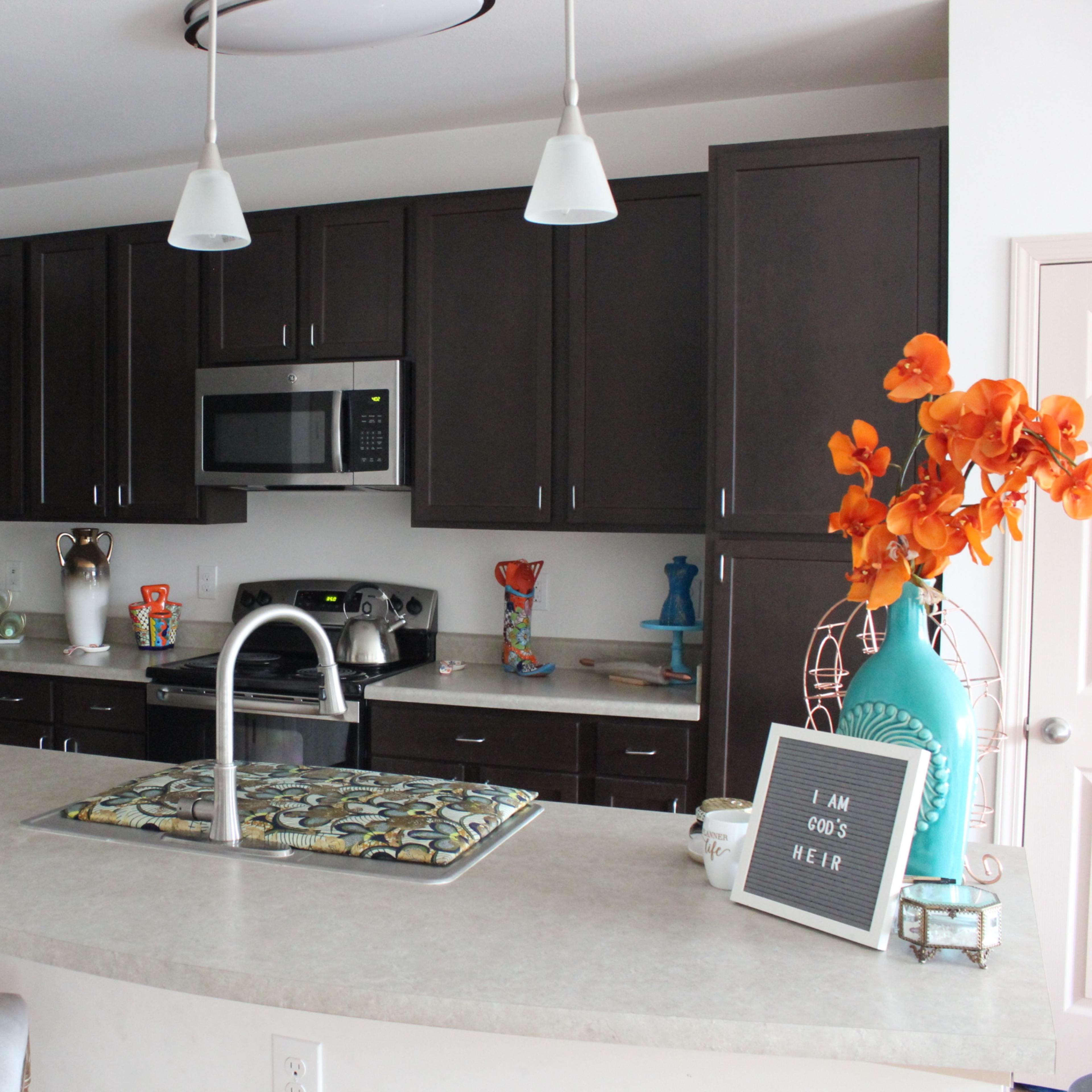 A modern kitchen with dark cabinets, stainless steel appliances, and a central island featuring decorative items and a vase of orange flowers.
