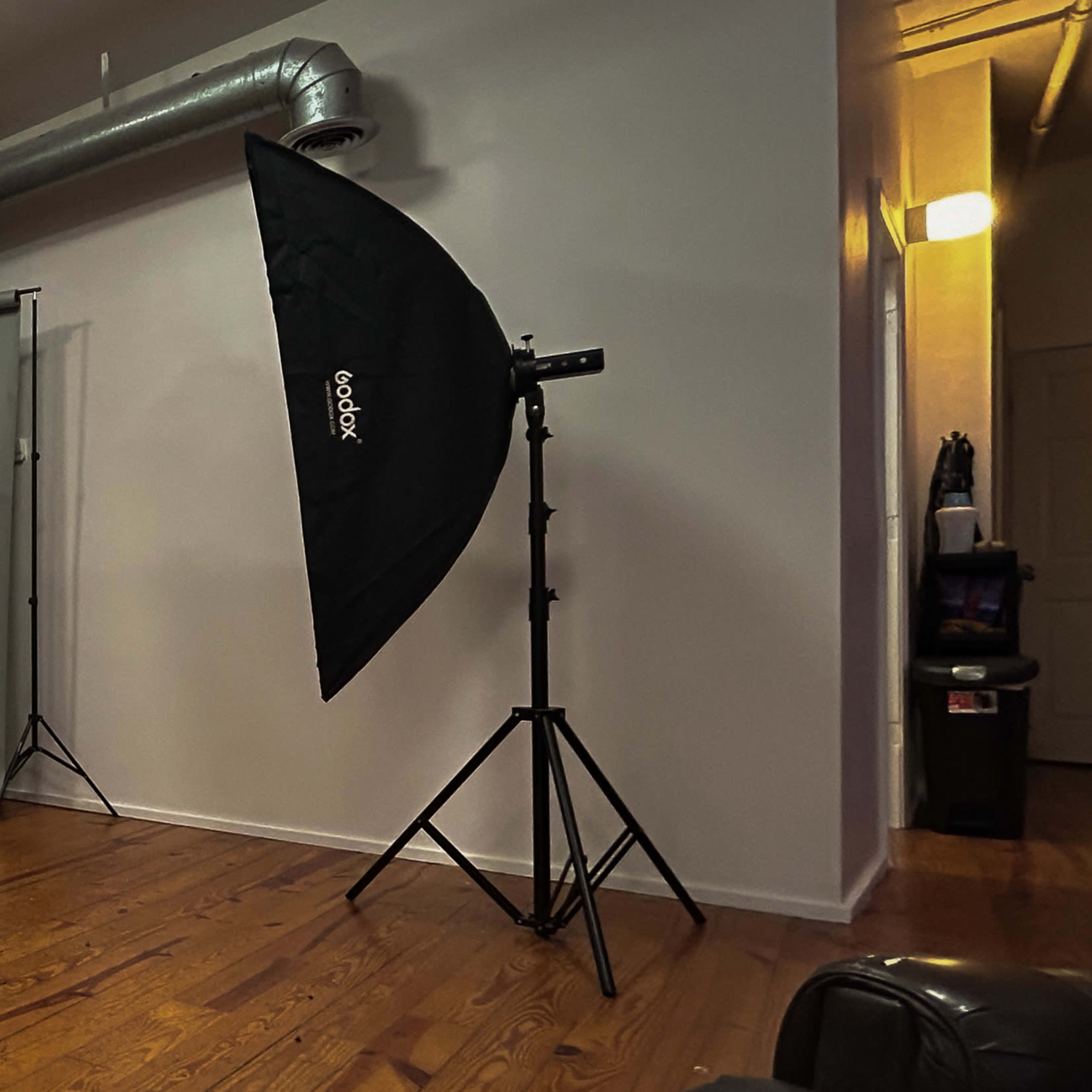 A photography studio with two large softbox lights, a backdrop stand with a gray backdrop, and a folding chair on a wooden floor.