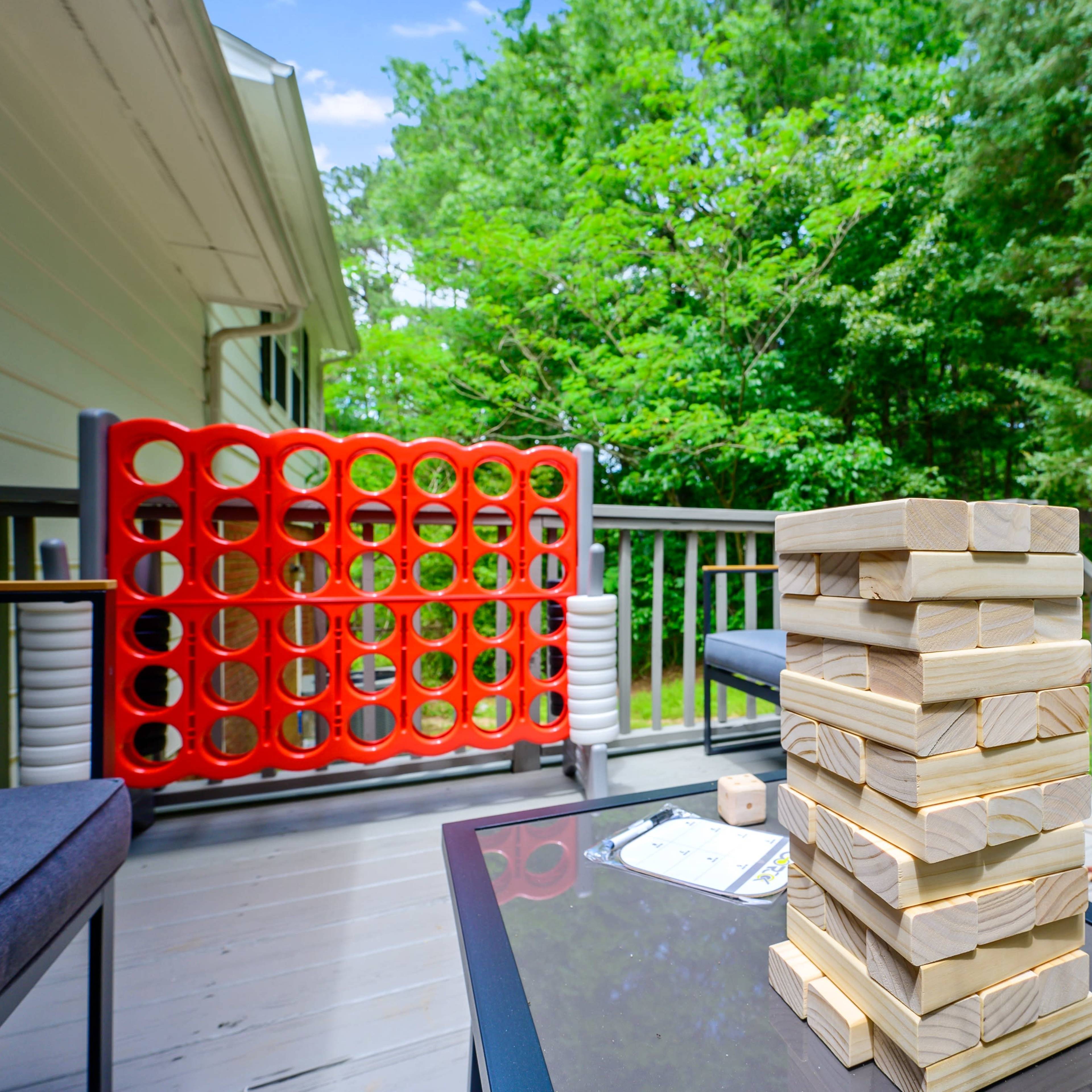A wooden deck features a Jenga tower, a Connect Four game, and two seating areas surrounded by trees.