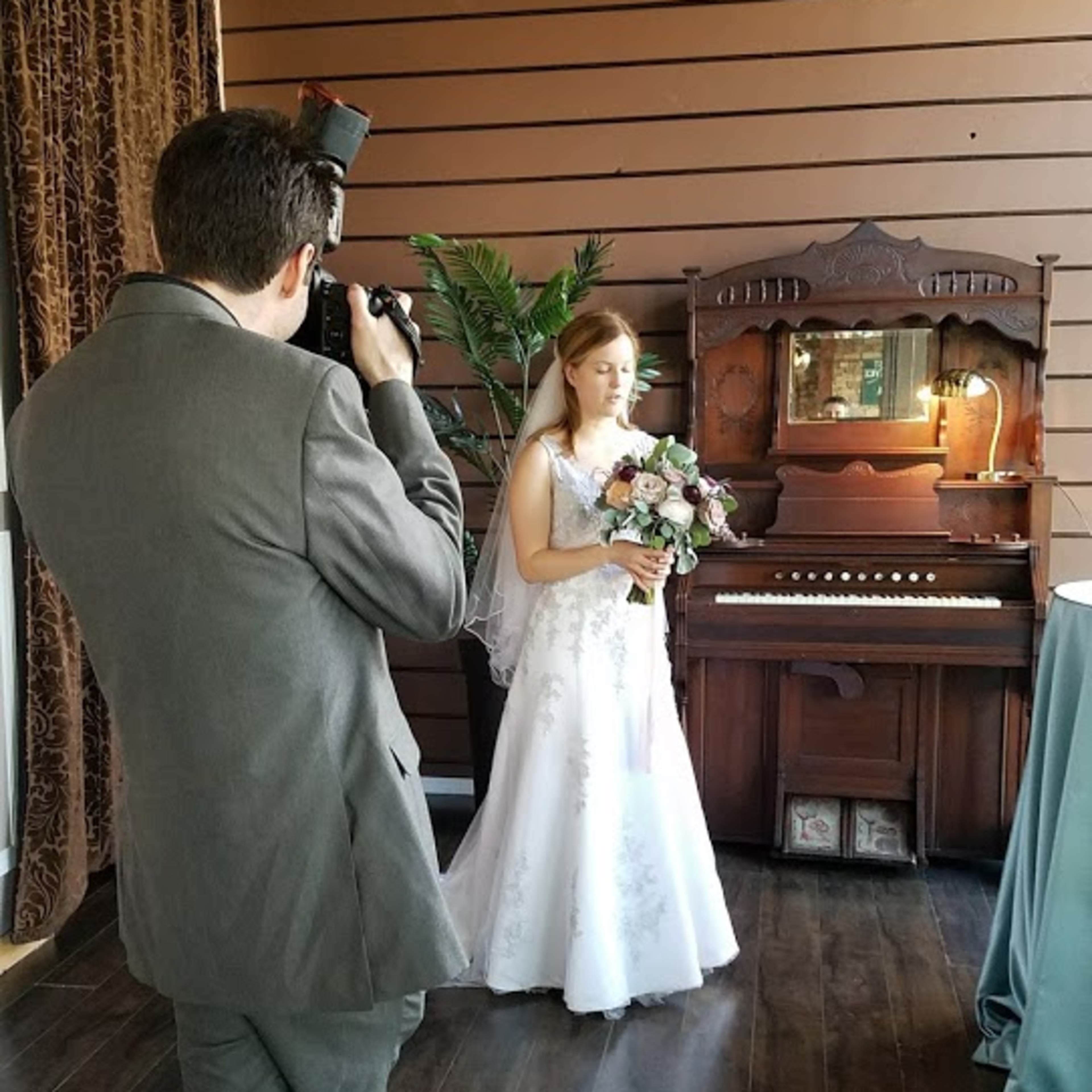 A bride in a white gown poses with a bouquet while a photographer captures the moment in a decorated indoor setting.