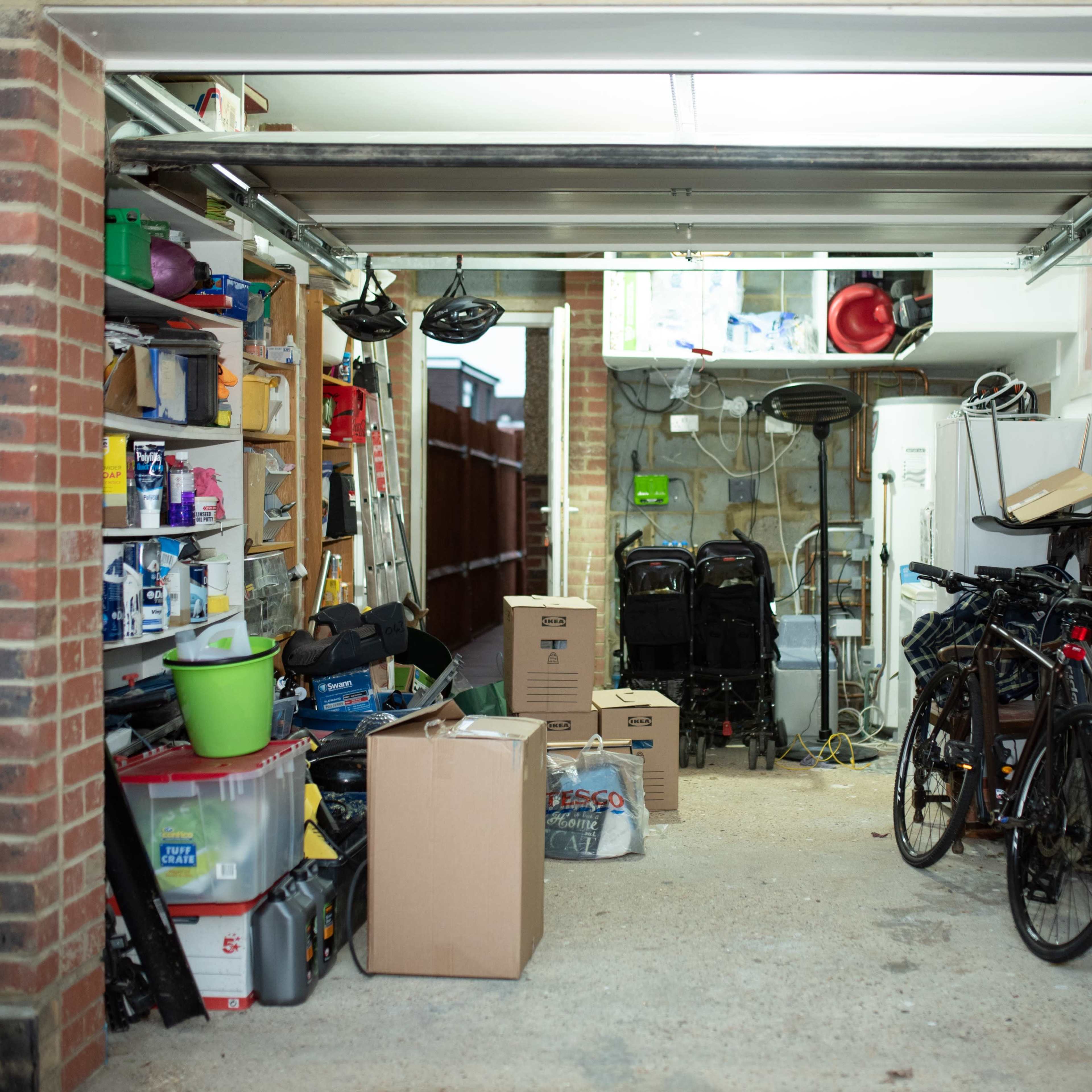 A cluttered garage with bicycles, boxes, and various storage items lining the walls.