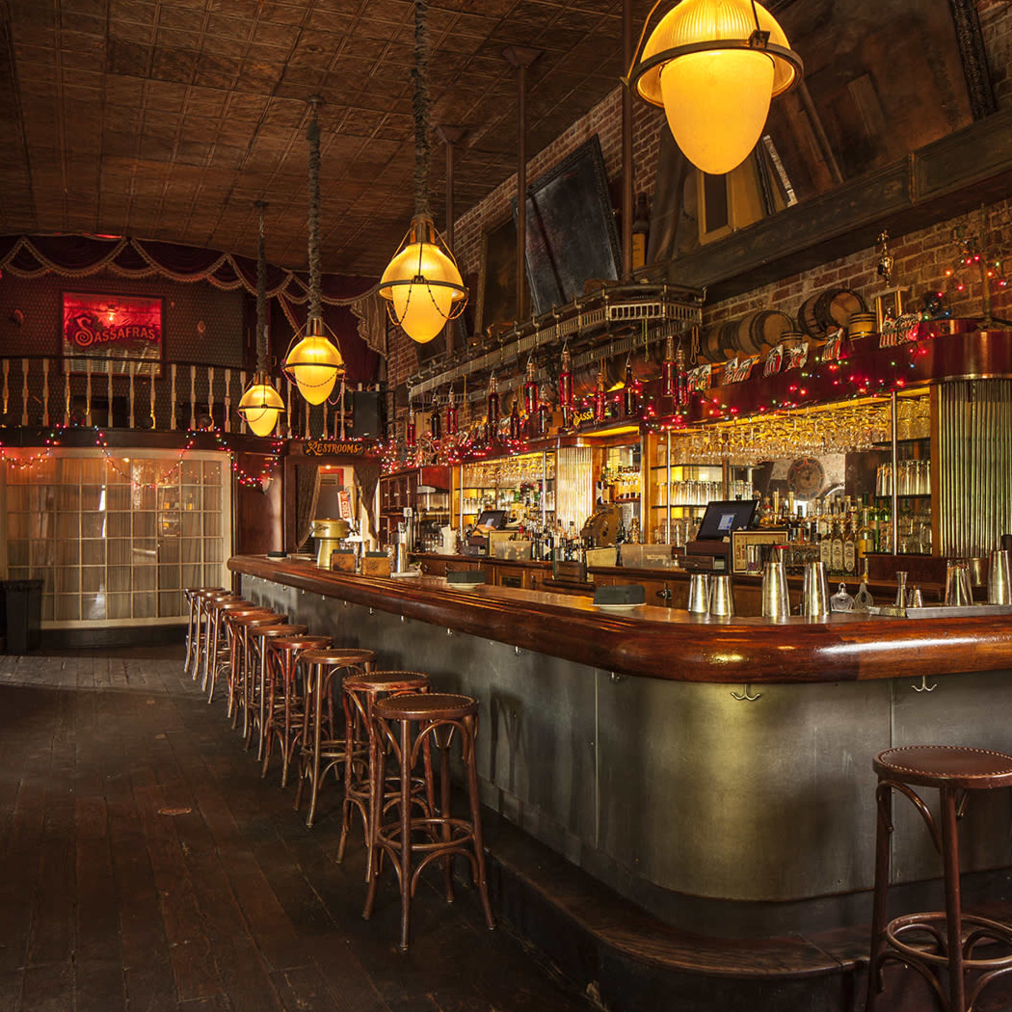 A vintage-style bar with wooden flooring, a long curved bar counter, and warm lighting fixtures, lined with high stools.
