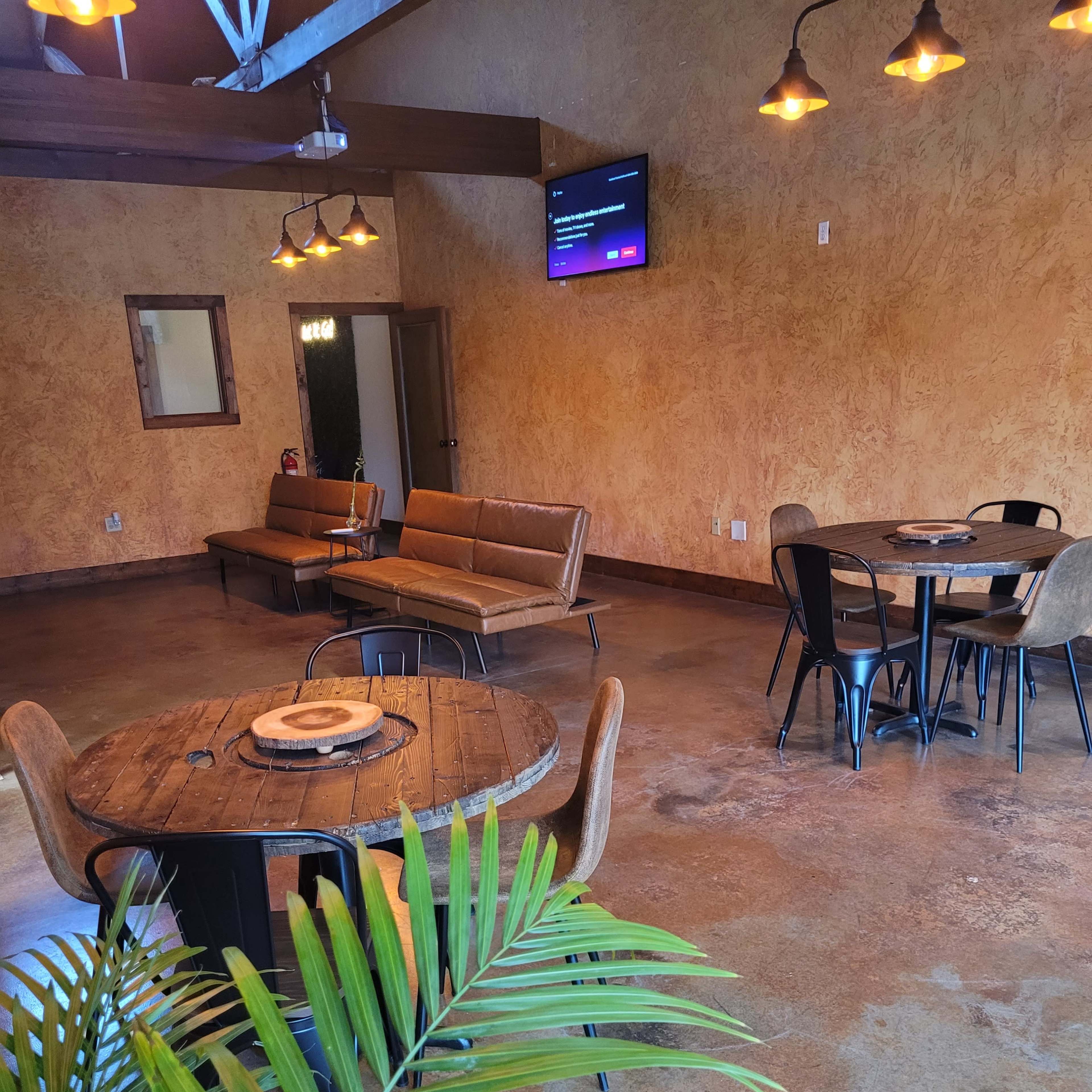An indoor seating area featuring two tables, chairs, a couch, and decorative lighting against a textured wall.