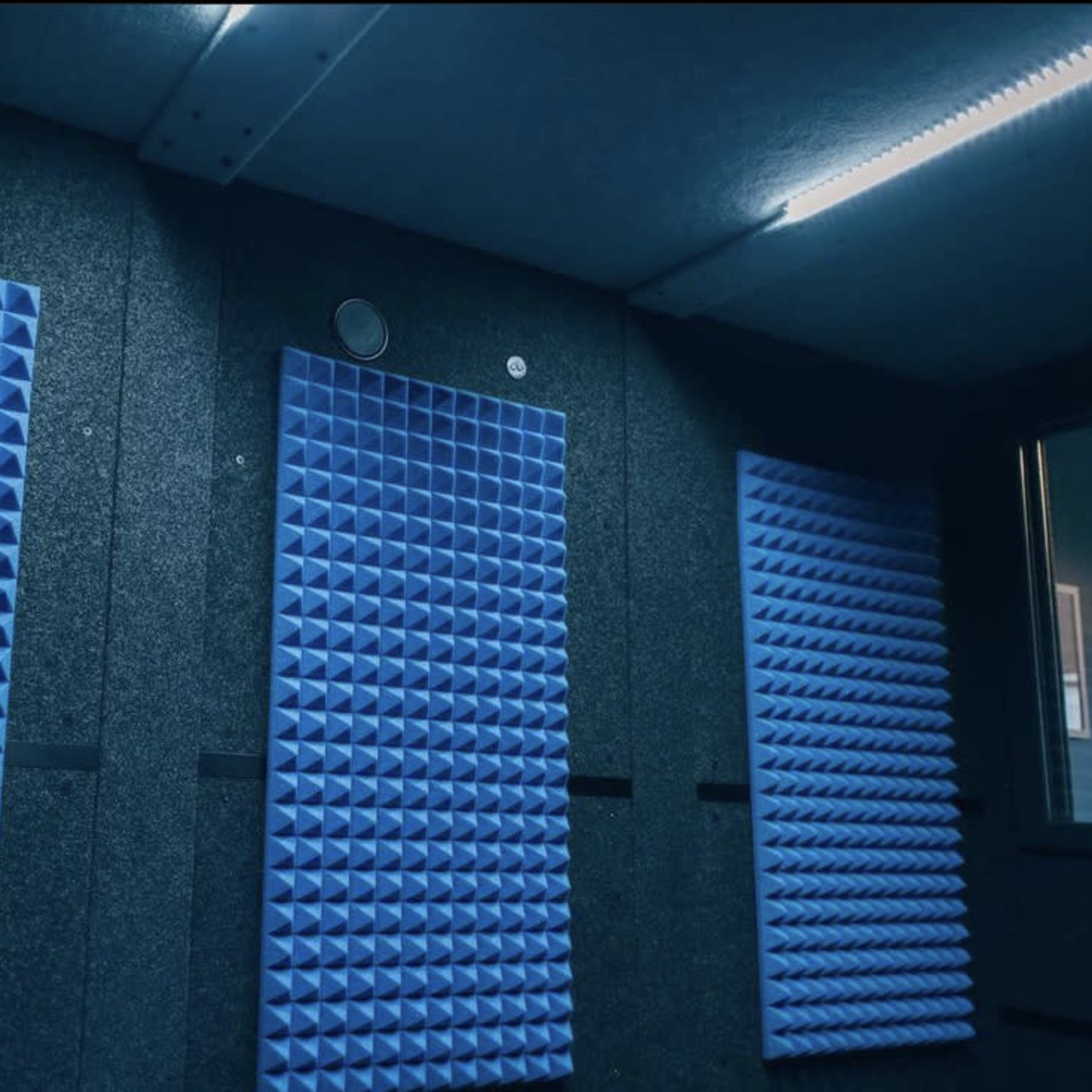 A soundproof room with three blue acoustic panels mounted on gray walls.