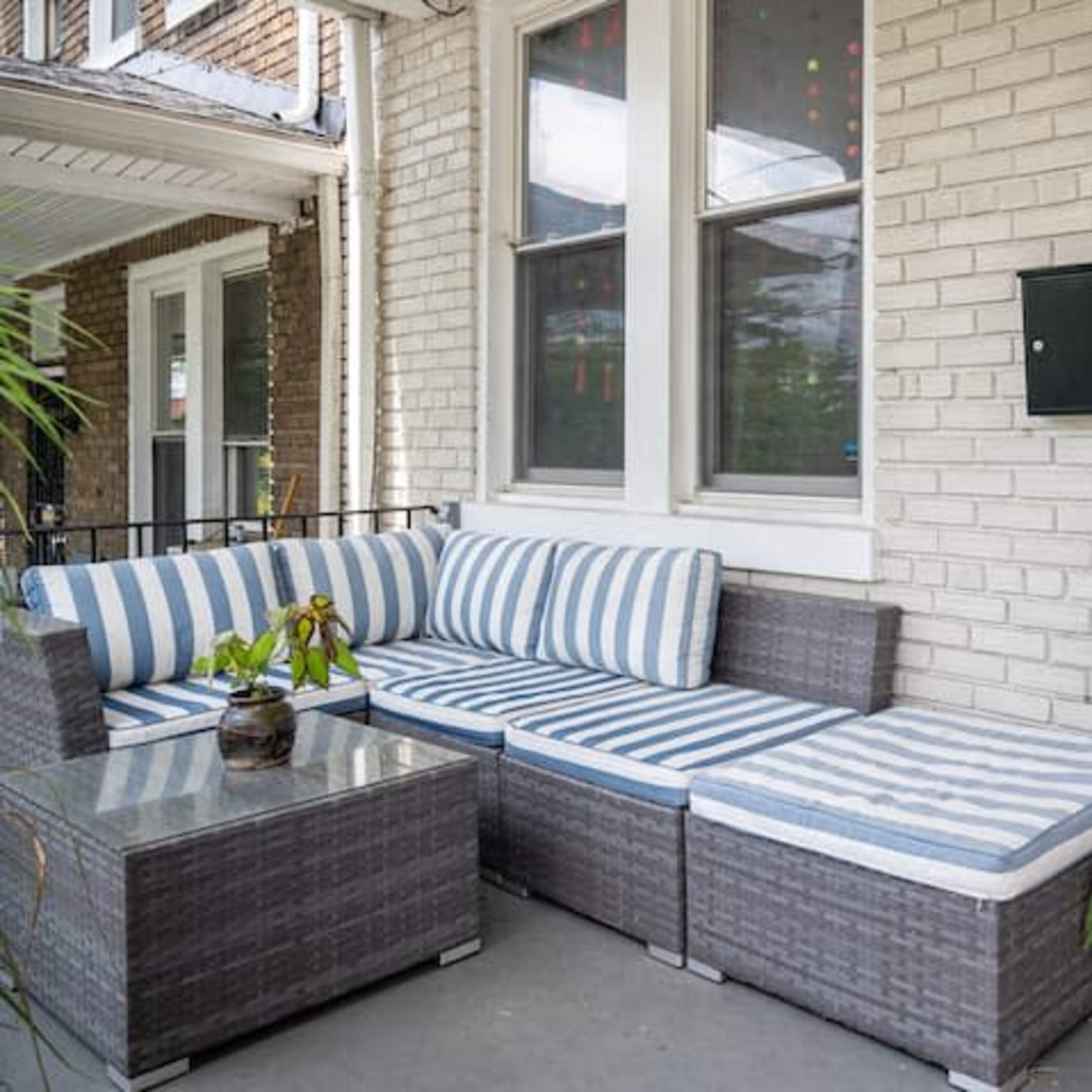 A front porch features a sectional couch with striped cushions, a glass-topped table, and a potted plant beside a red door.