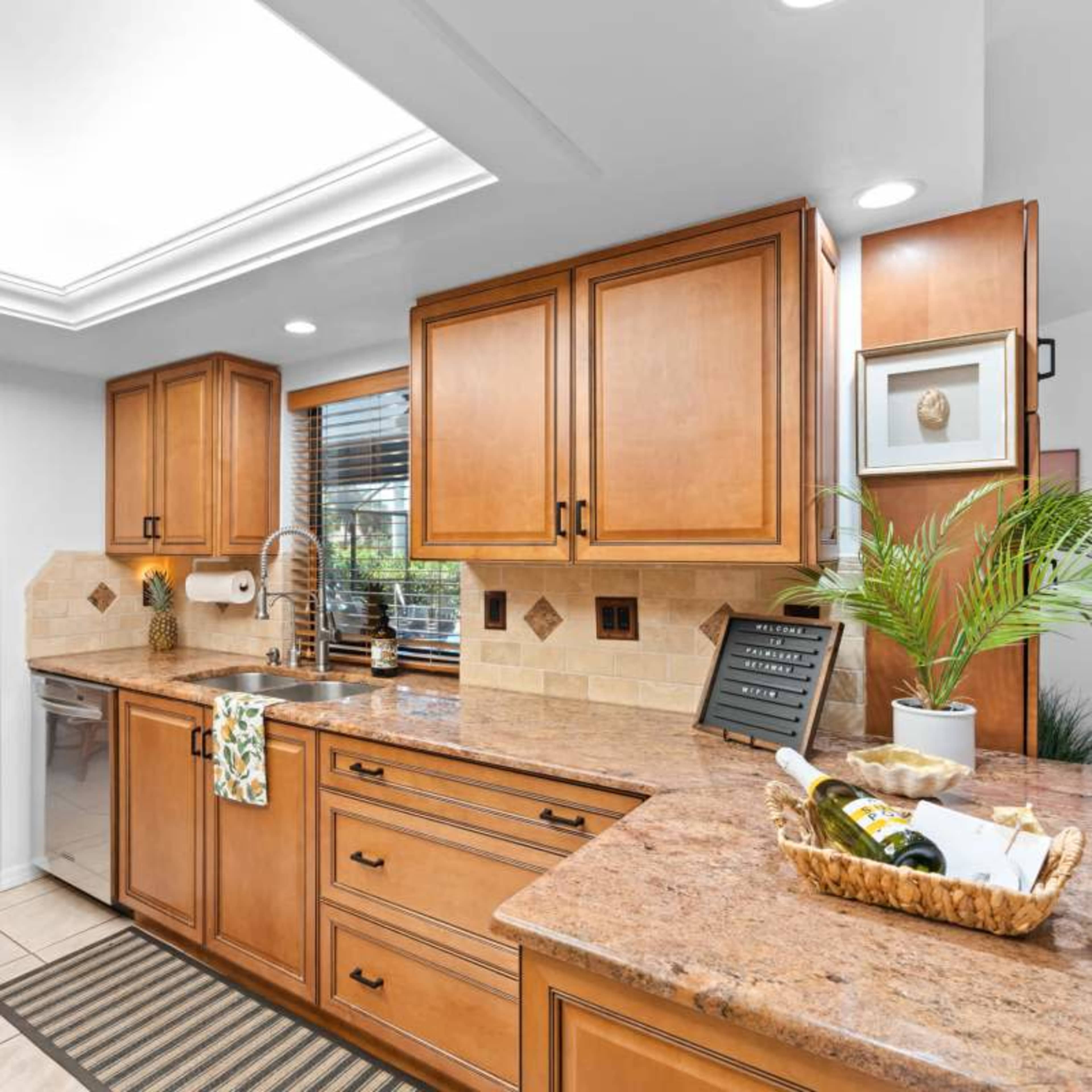 A modern kitchen with wooden cabinets, a granite countertop, and a decorative arrangement of plants and a wine basket.