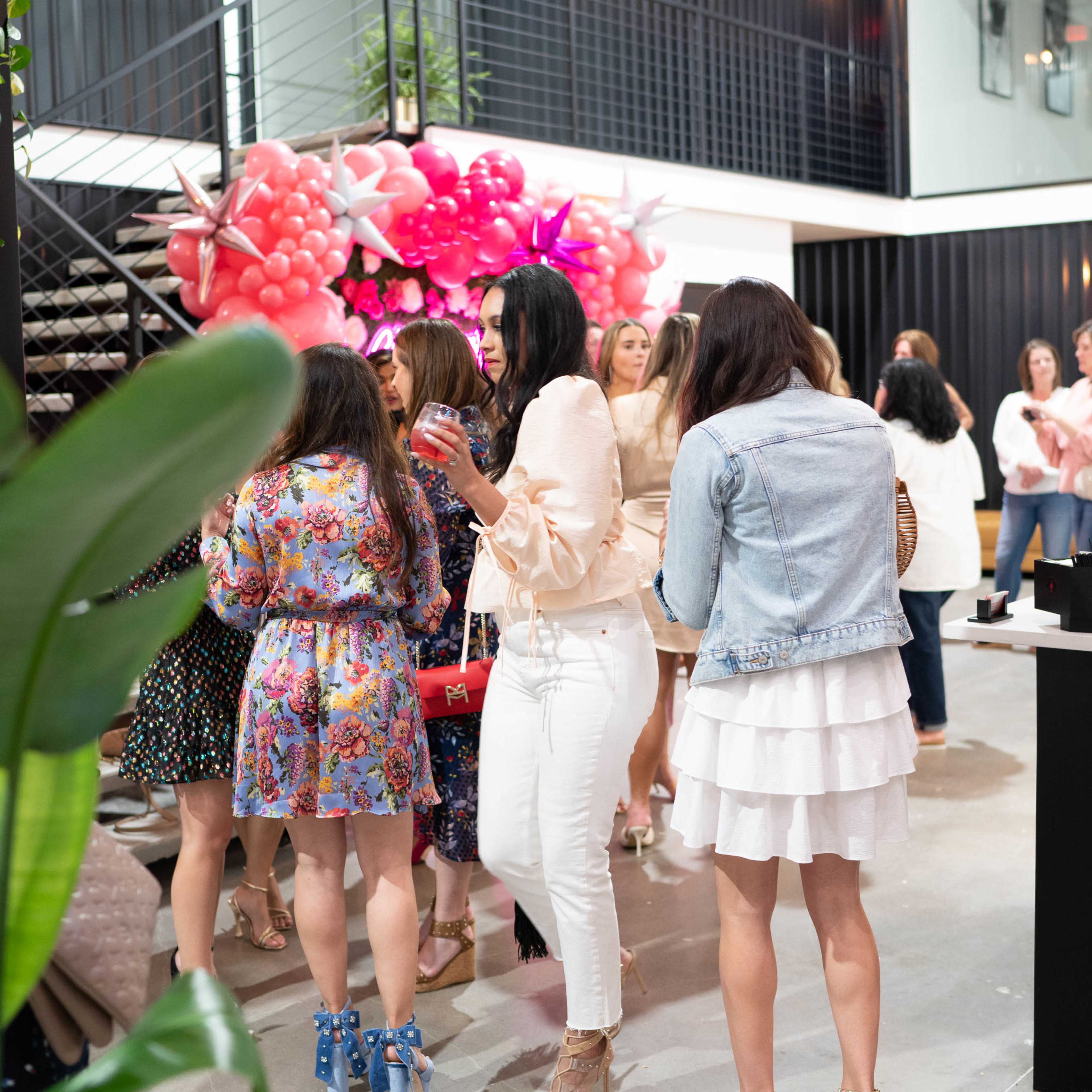 A group of women socialize near a colorful balloon arch in a modern indoor space.