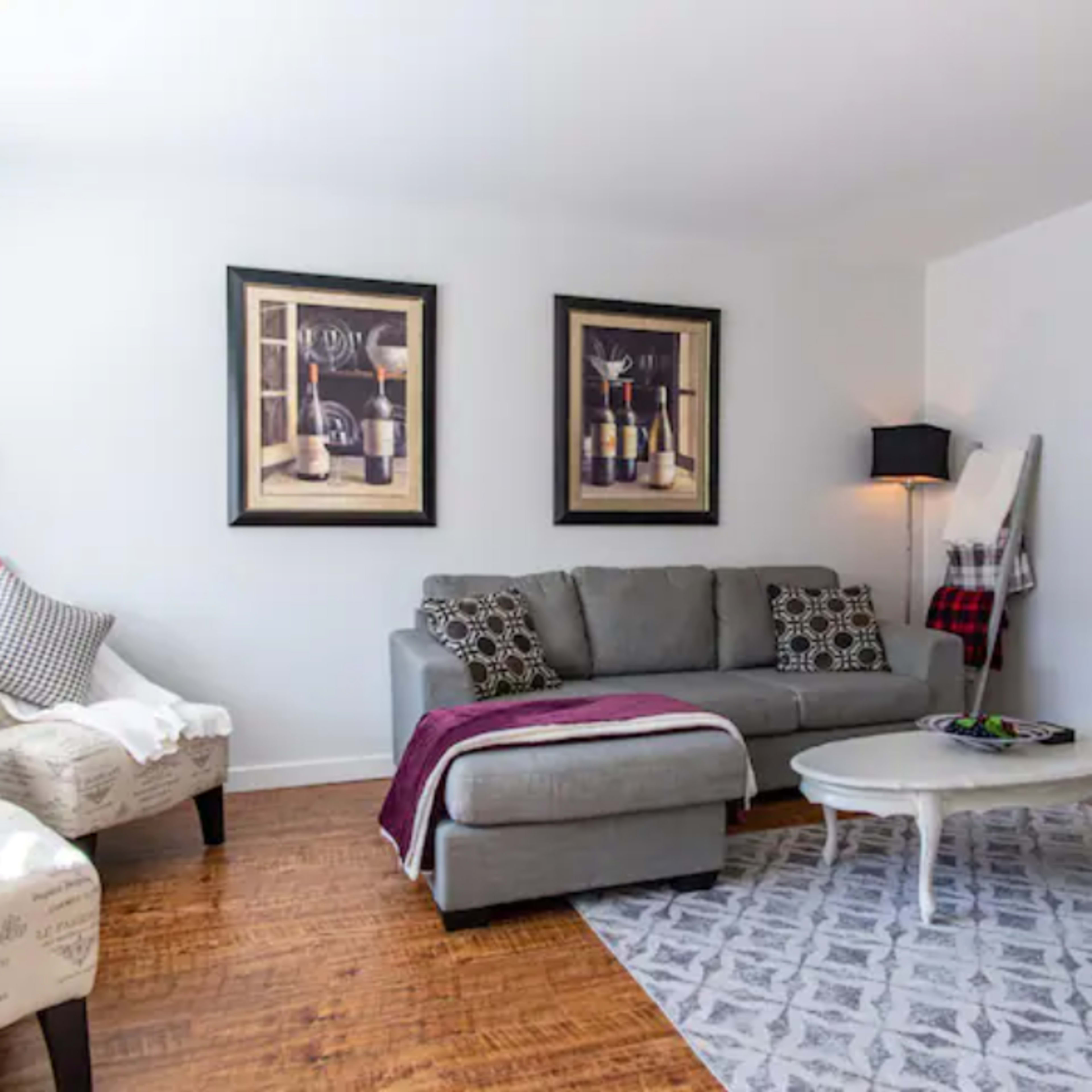 The living room features a gray sofa with a throw blanket, two patterned chairs, a round coffee table, and framed artwork on the walls.