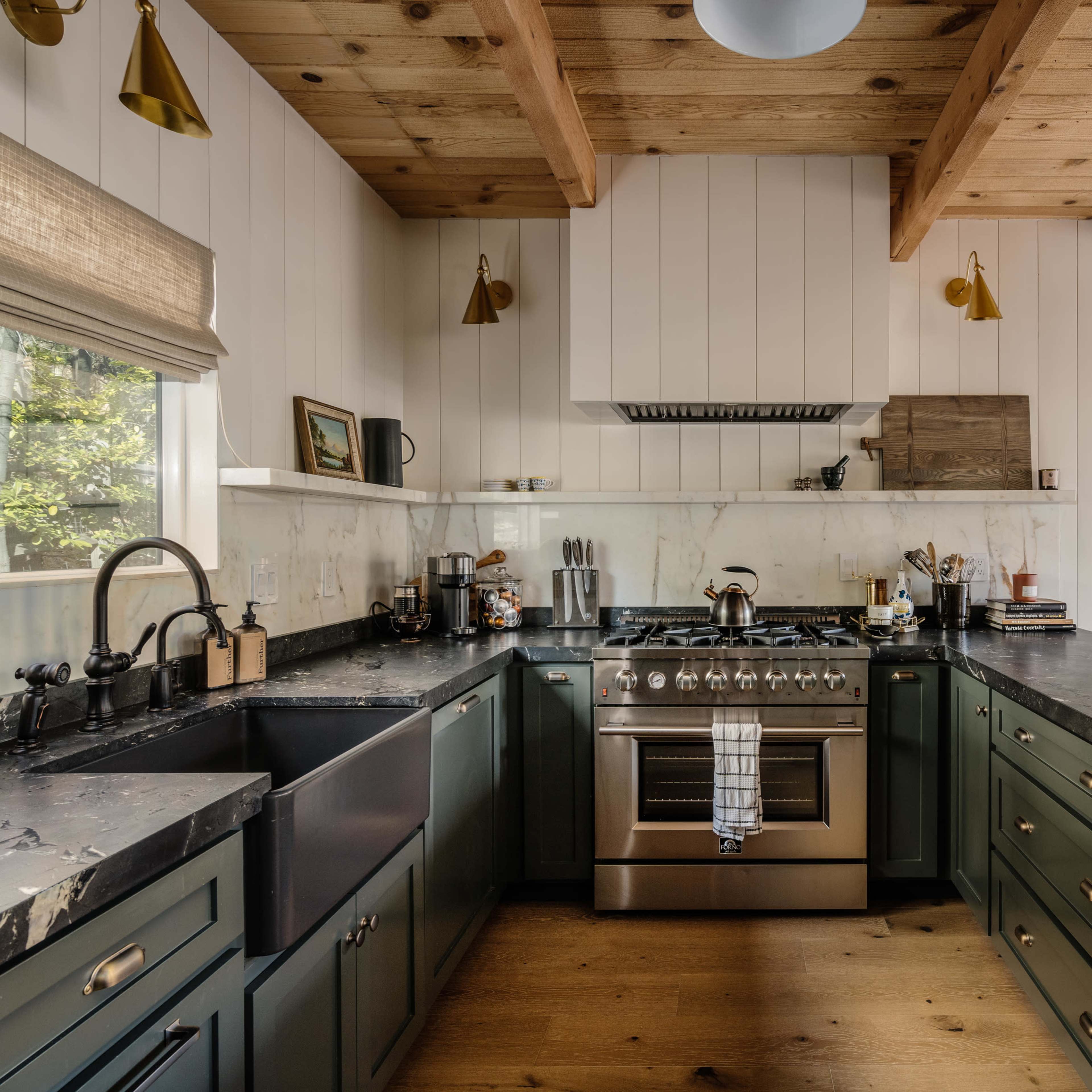 A modern kitchen with dark green cabinetry, a stainless steel stove, and wooden beams overhead.