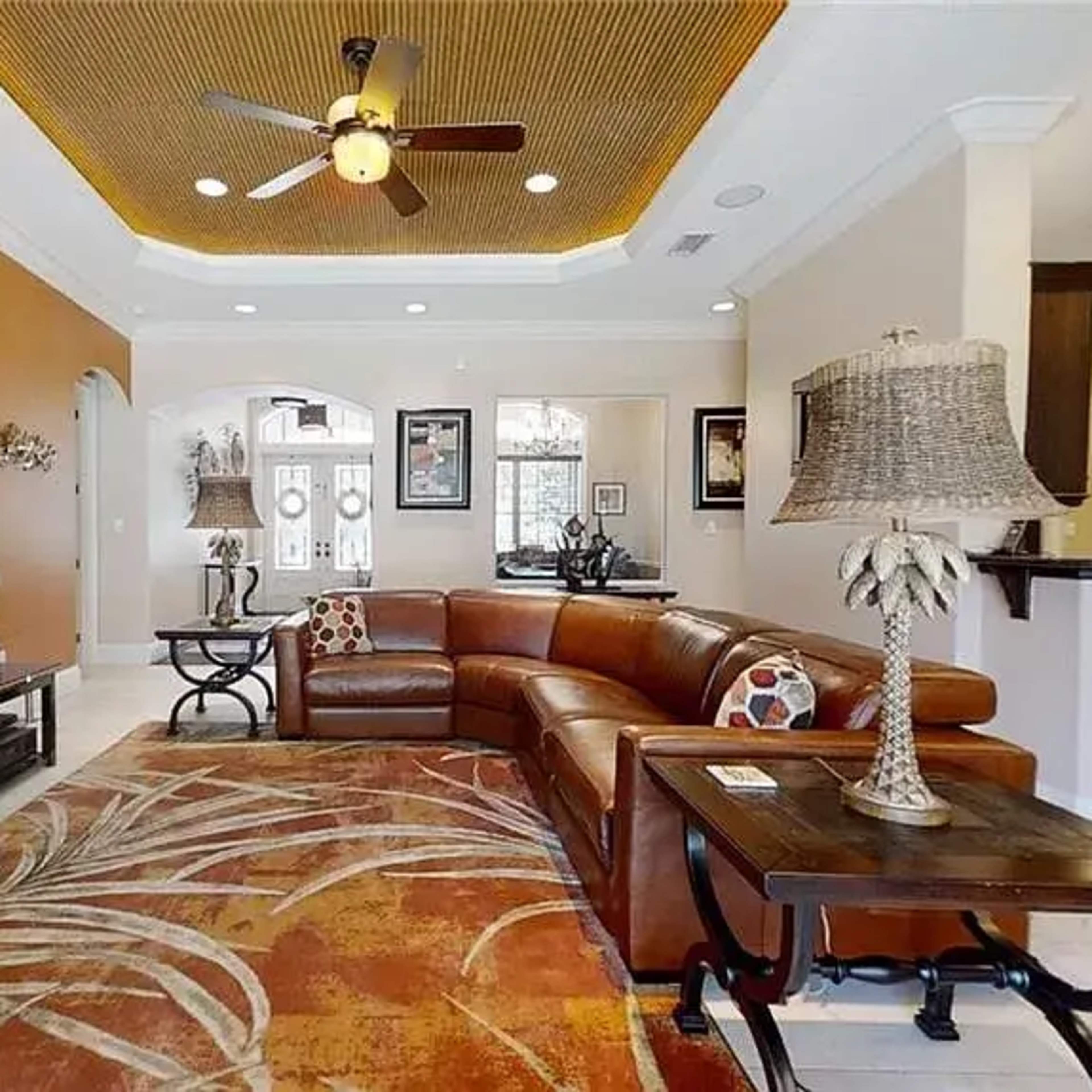 The living room features a brown sectional sofa arranged around a patterned area rug, with an orange accent wall and a ceiling fan above.
