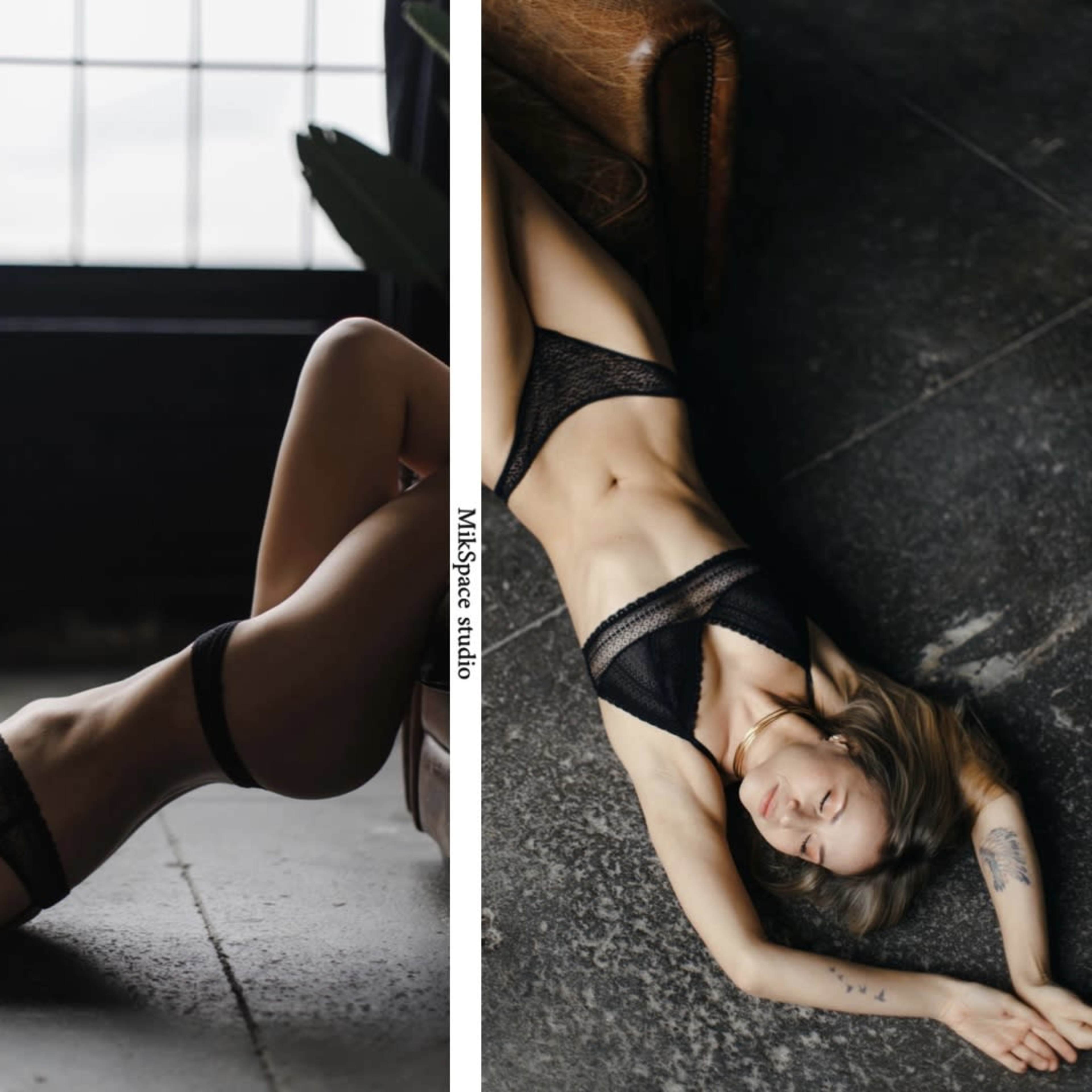 A woman in black lingerie poses on the floor and a chair in a dimly lit, industrial-style room.