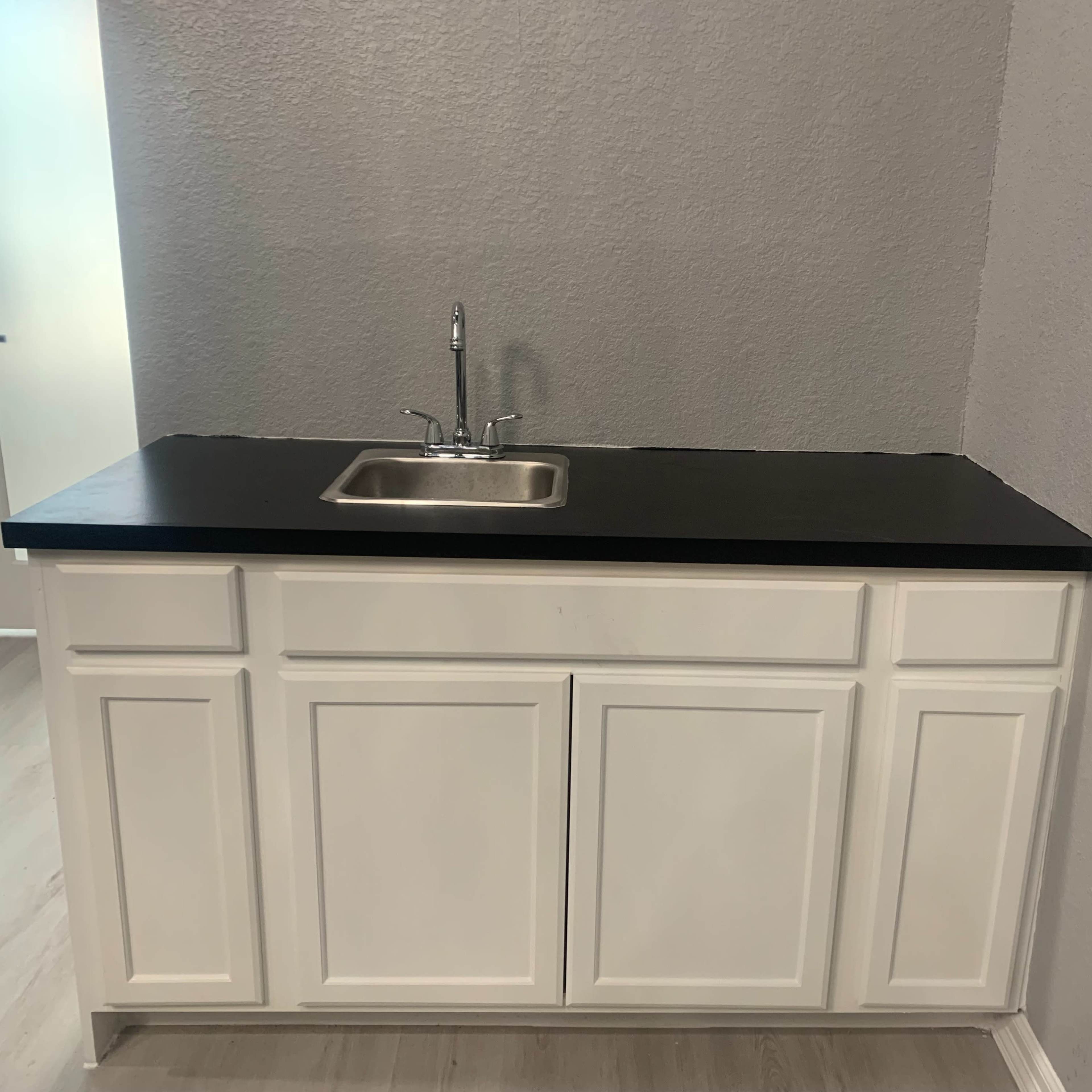 A white cabinet with a black countertop and a stainless steel sink in a room with gray walls.