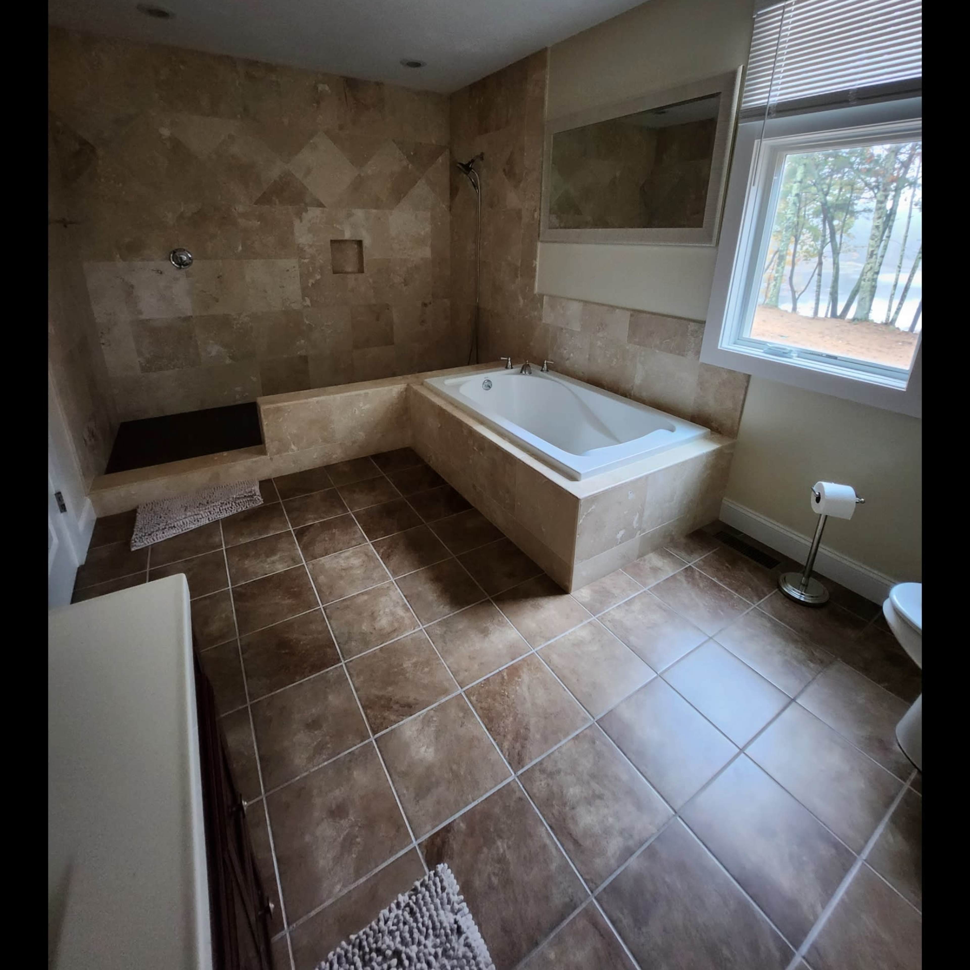 A spacious bathroom featuring a tiled floor, a large bathtub, and a window allowing natural light.