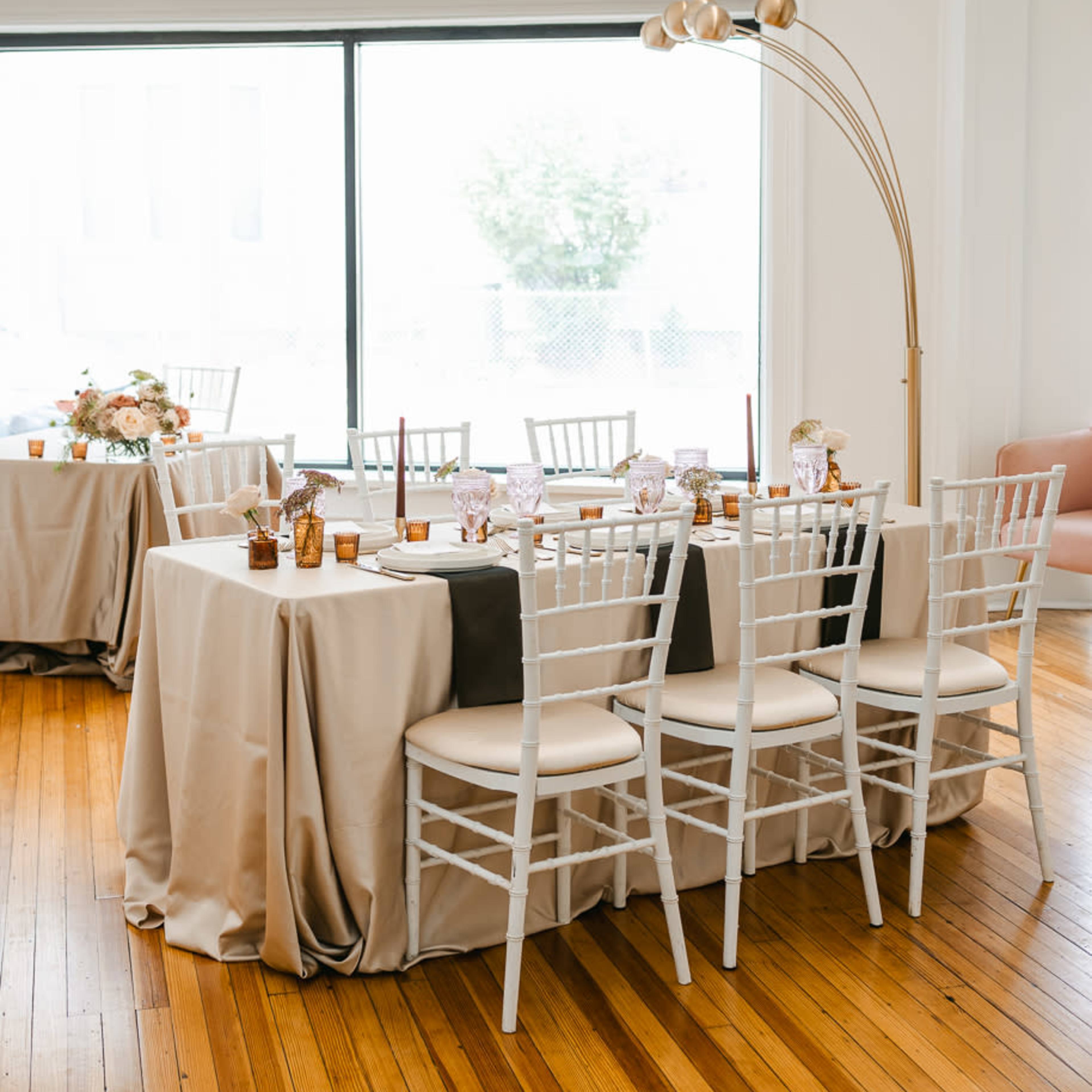 A well-decorated event space features elegantly set tables with light-colored tablecloths and decorative centerpieces.