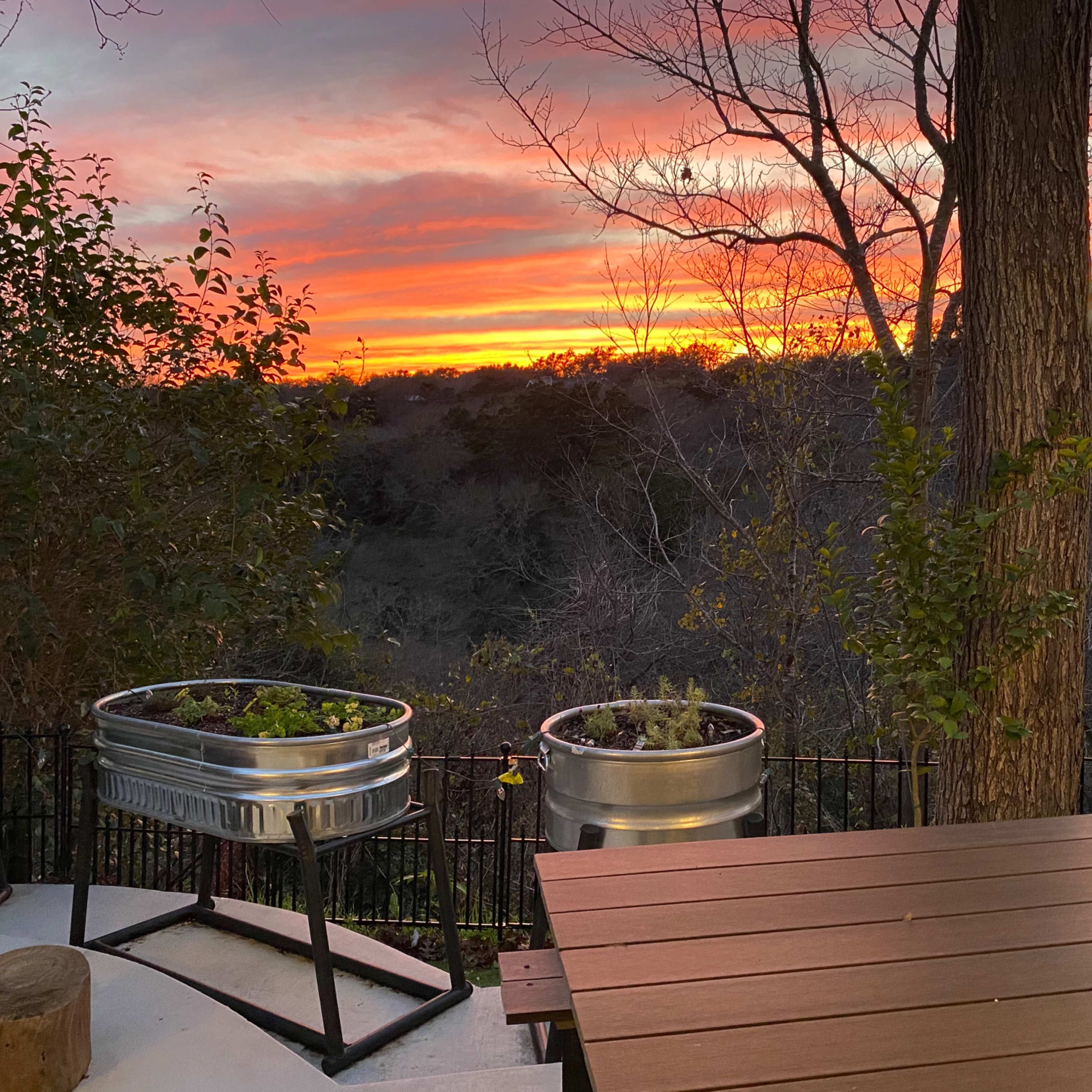 A sunset over a landscape, with metal planters and a wooden table in the foreground.