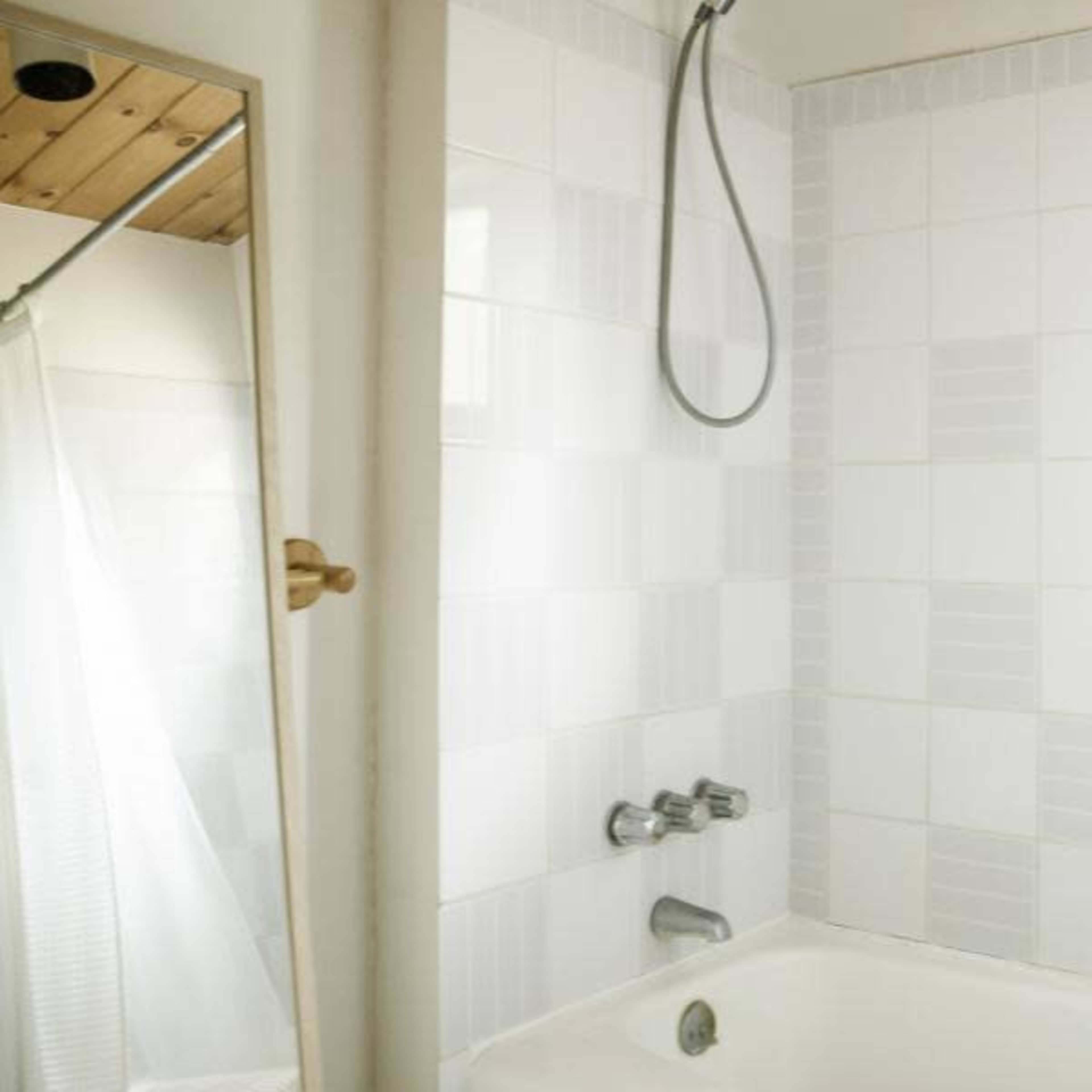 A clean bathroom with a shower enclosed by a curtain, a bathtub, and a window letting in natural light.