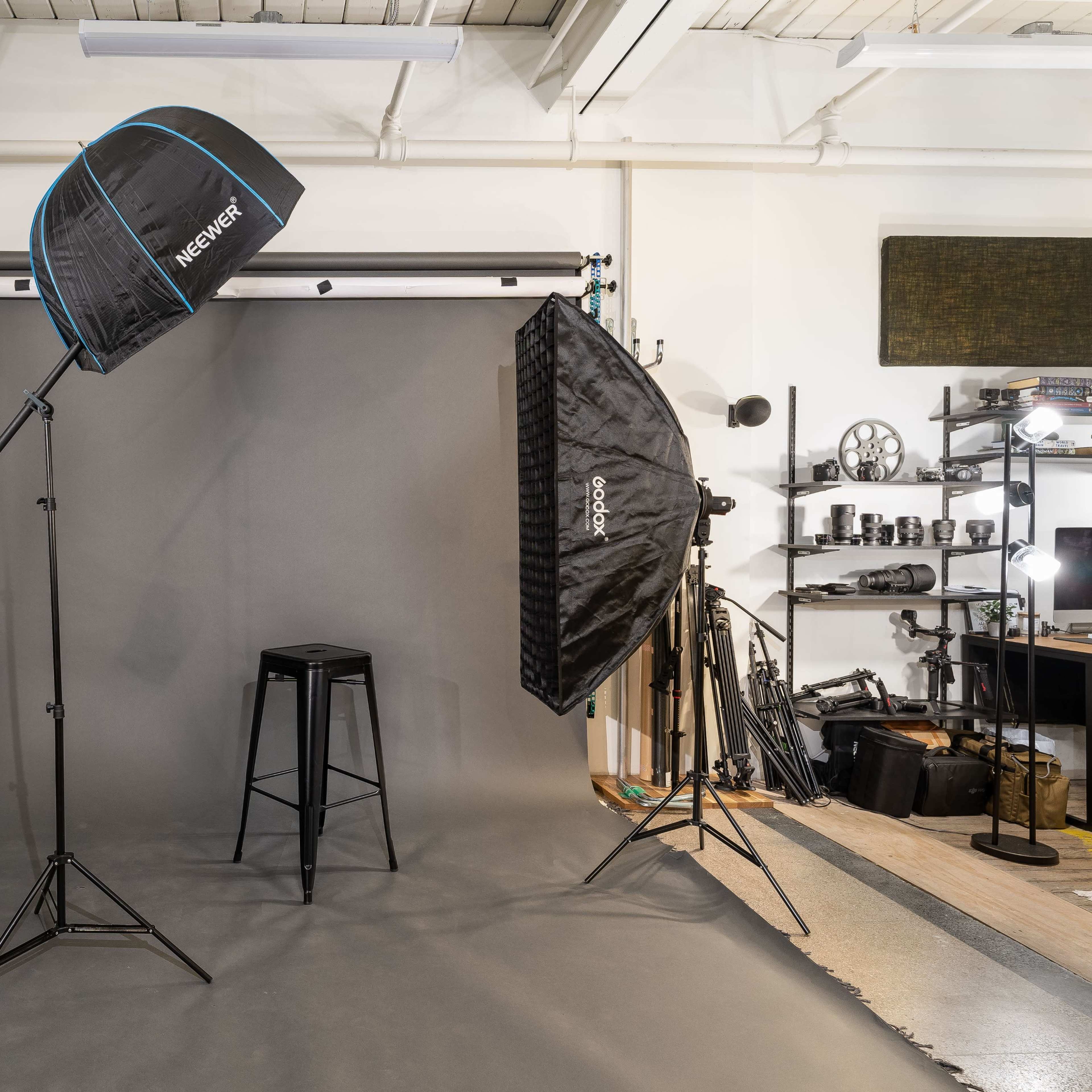 A photography studio setup with lighting equipment, a grey backdrop, and a stool positioned in the center.