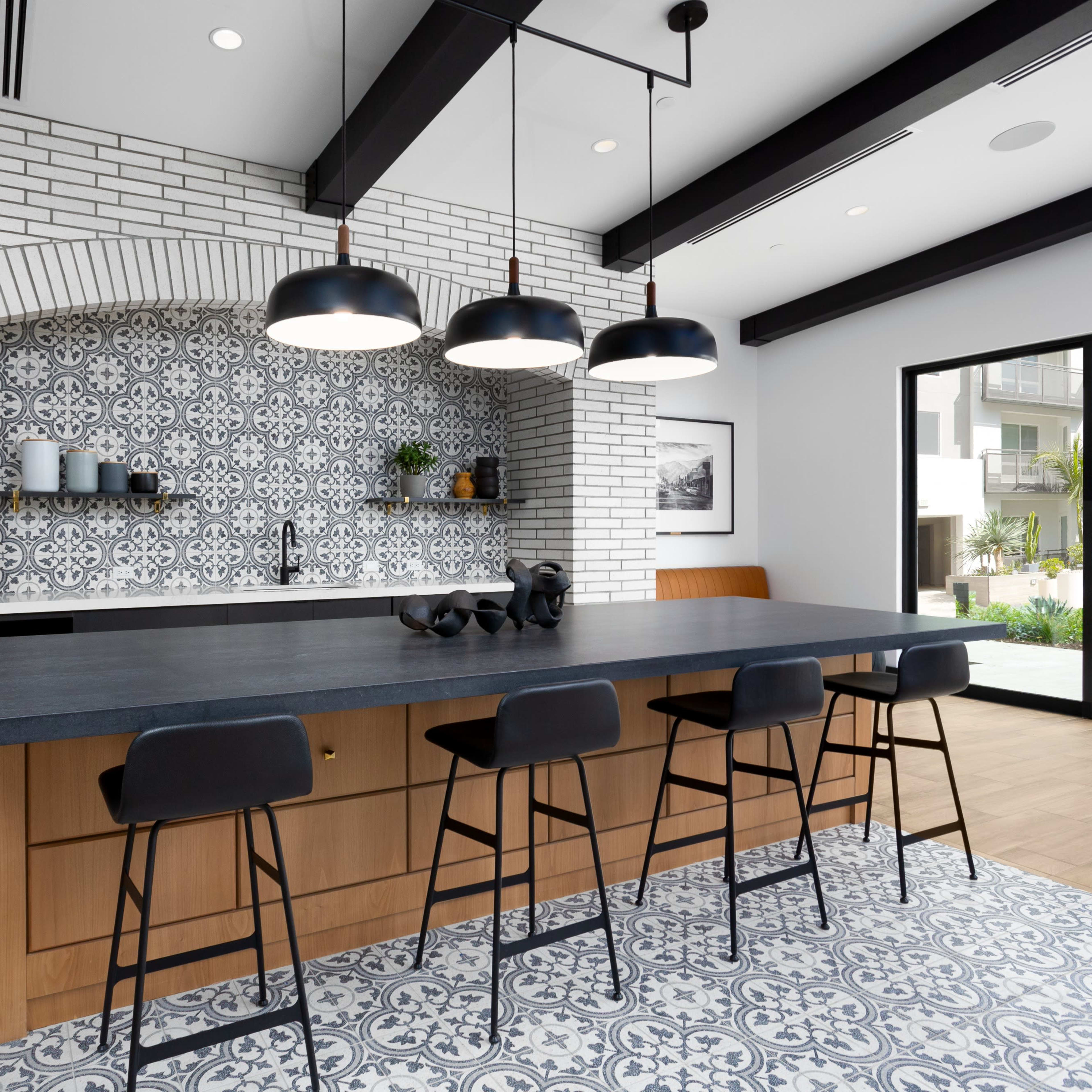 A modern kitchen features a large island with black bar stools, a patterned backsplash, and a sliding glass door that opens to an outdoor space.