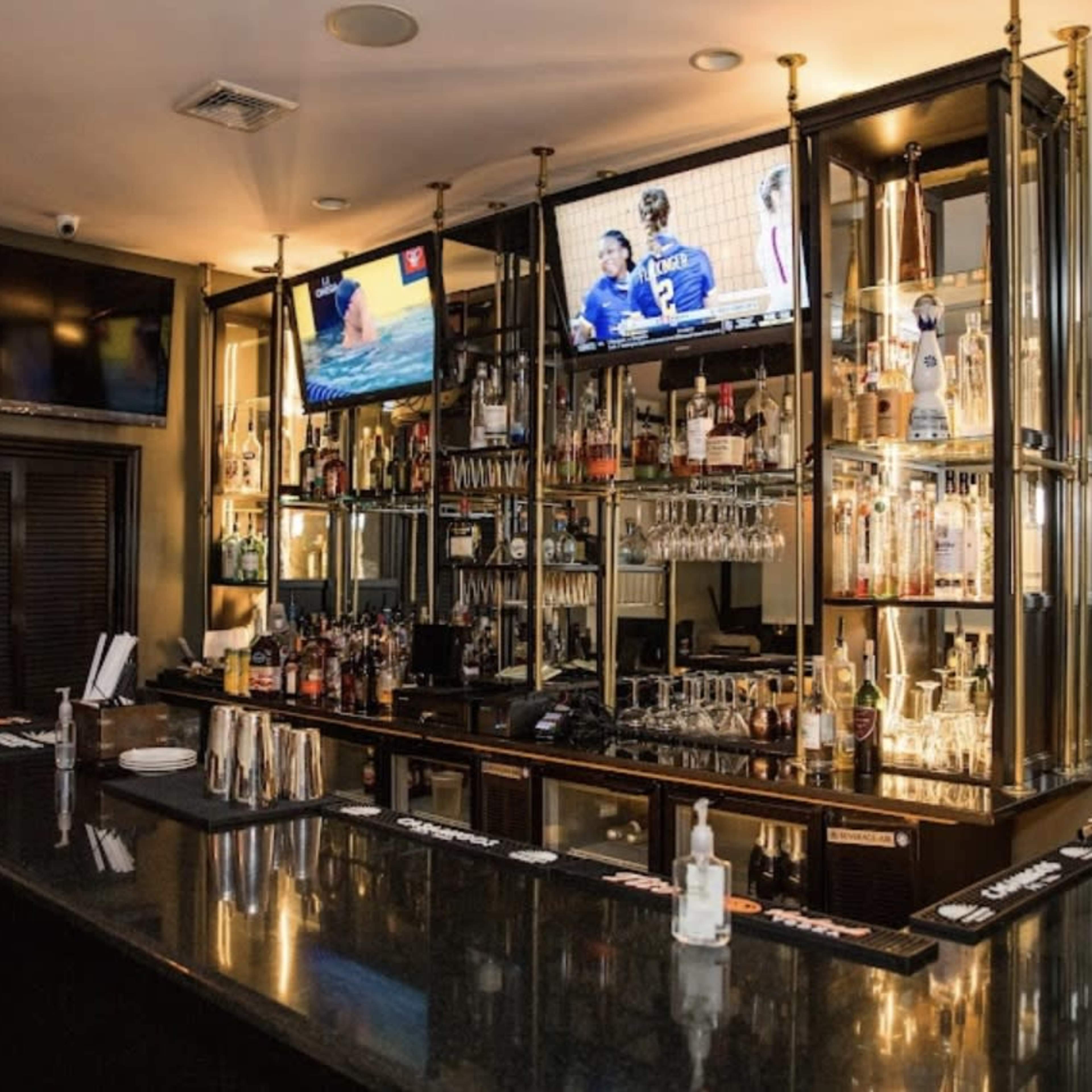A well-organized bar with a variety of liquor bottles displayed on shelves and two televisions mounted on the walls.