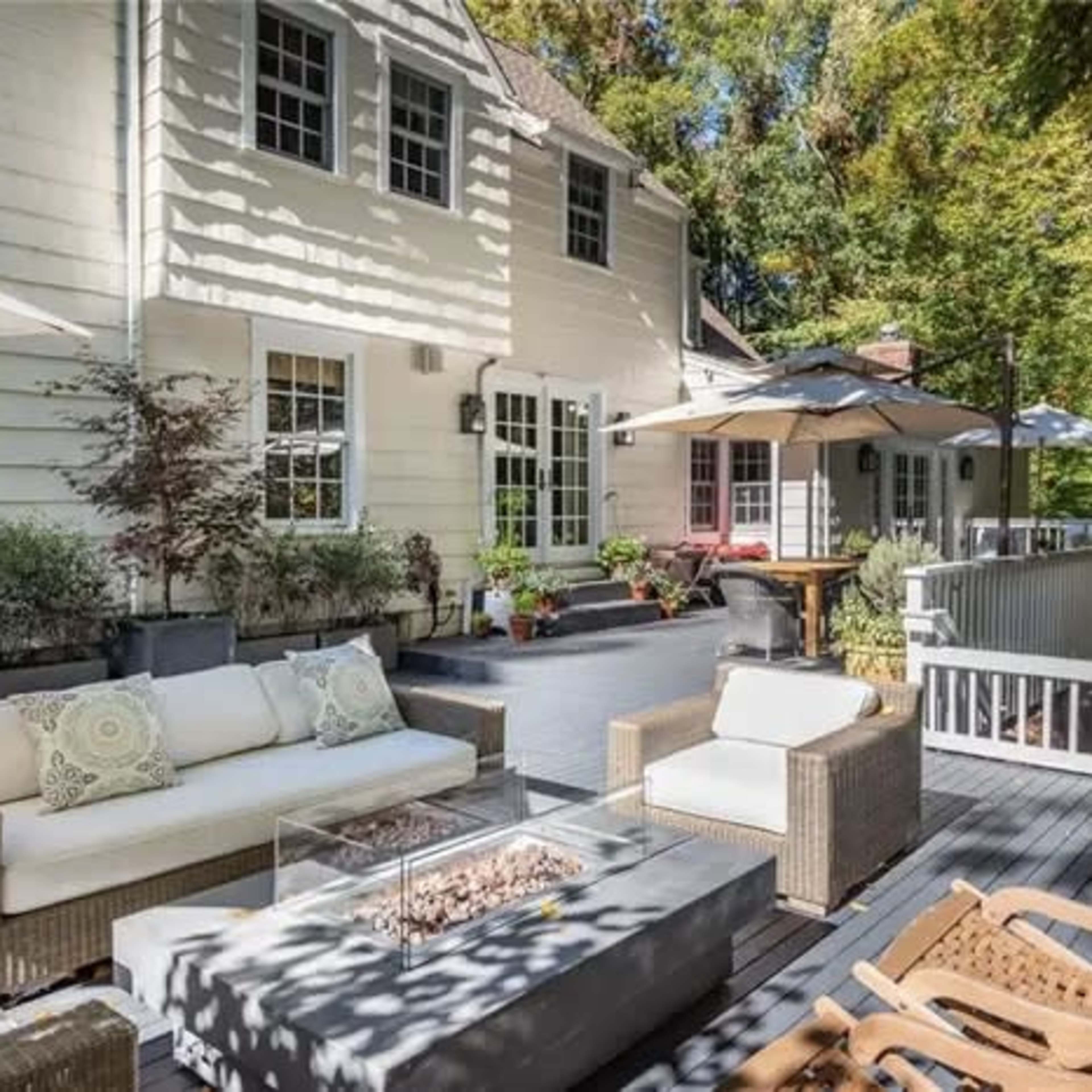 A spacious patio features a seating area with a fire pit, surrounded by plants and outdoor umbrellas.