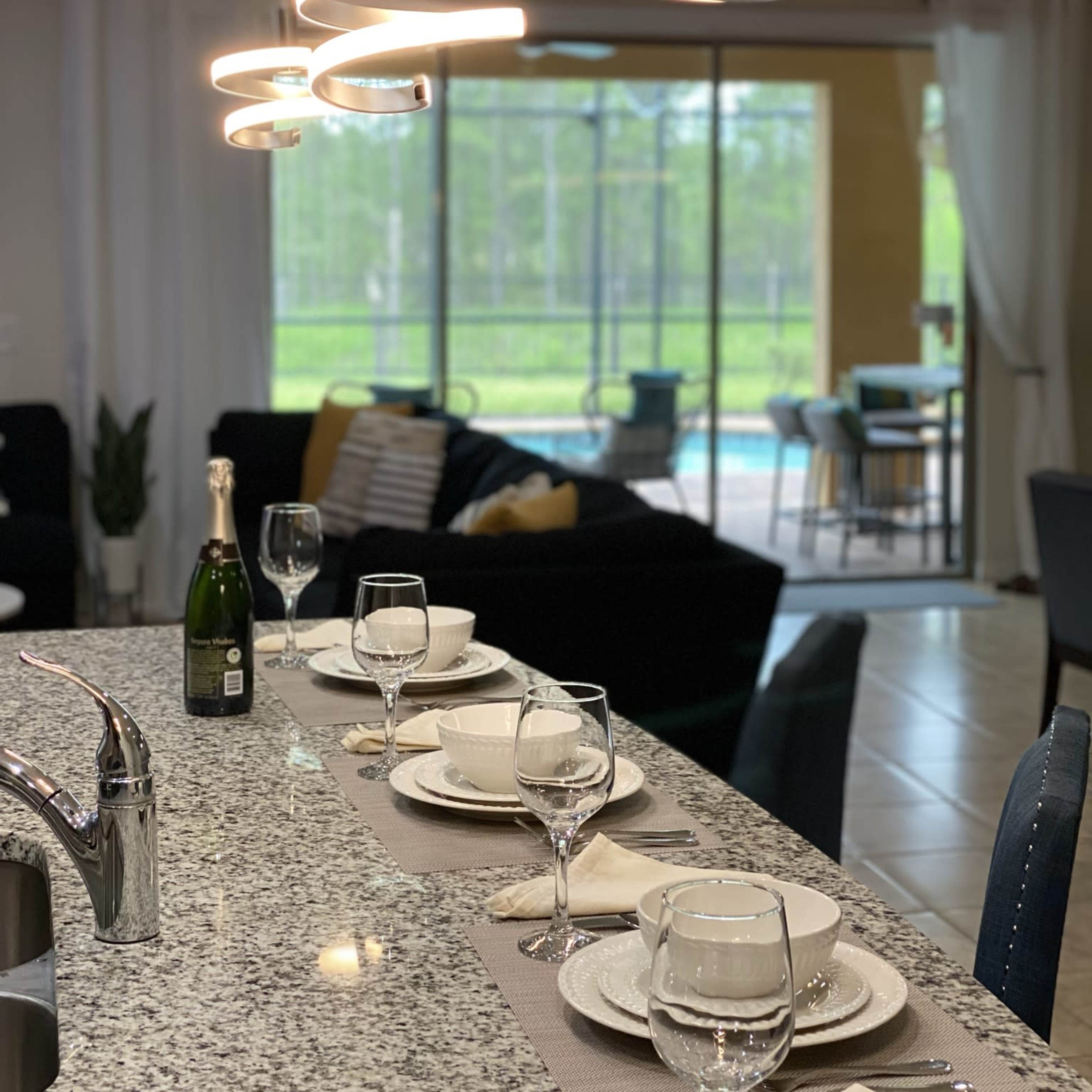 A sleek dining area features a modern table set for dinner, with glassware and plates arranged neatly, illuminated by contemporary light fixtures.