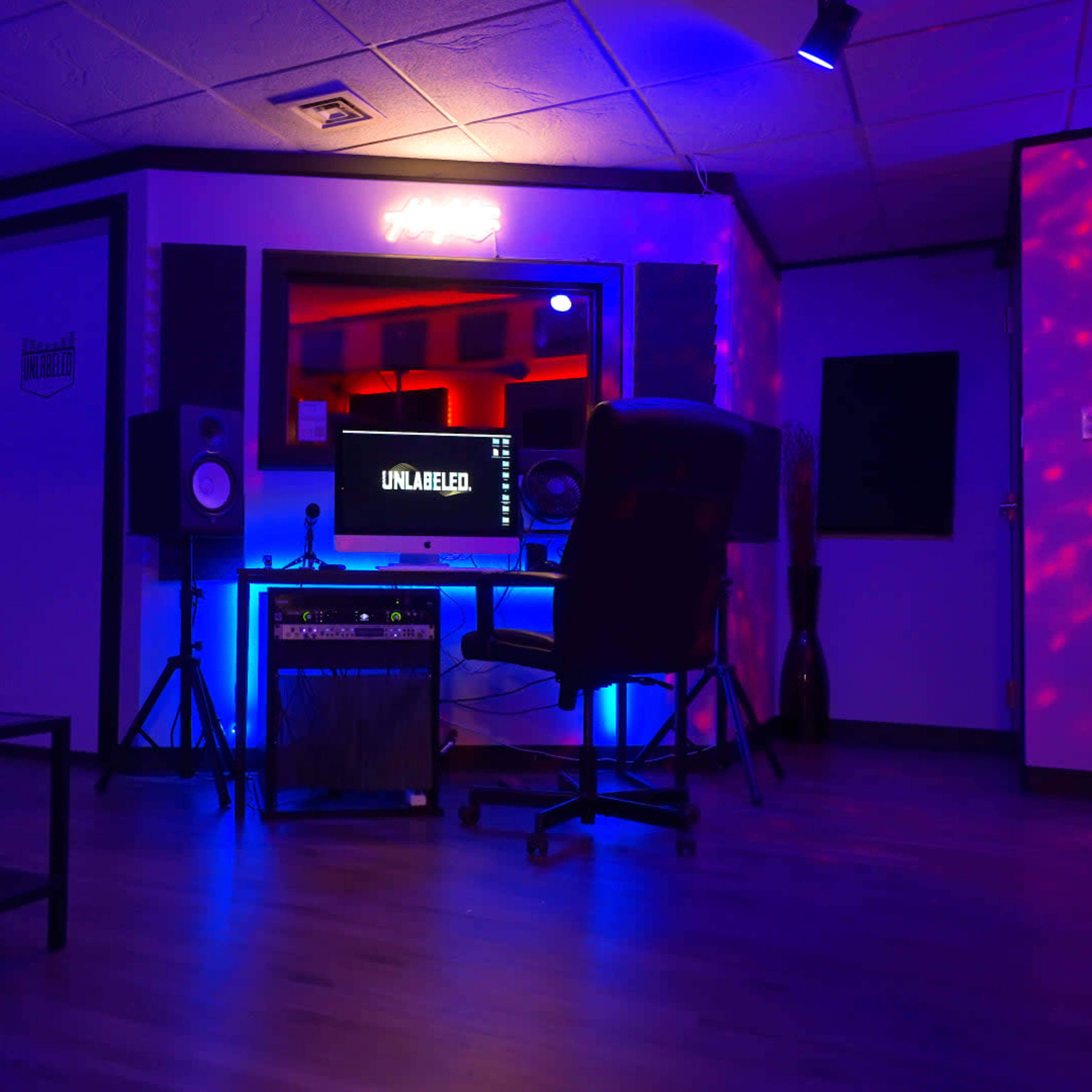 A music recording studio with a computer setup, speakers, and ambient lighting in shades of blue and red.