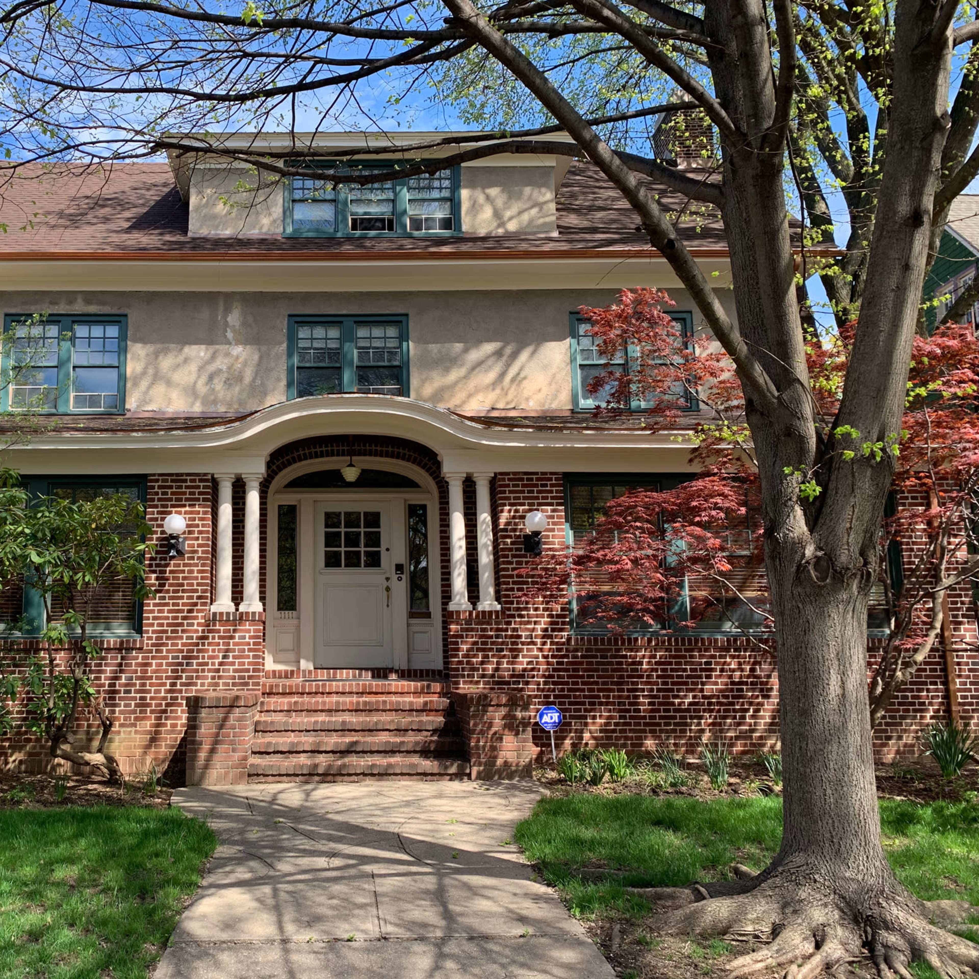 A large brick house with a tan upper facade, a front porch supported by white columns, and a neatly landscaped yard.