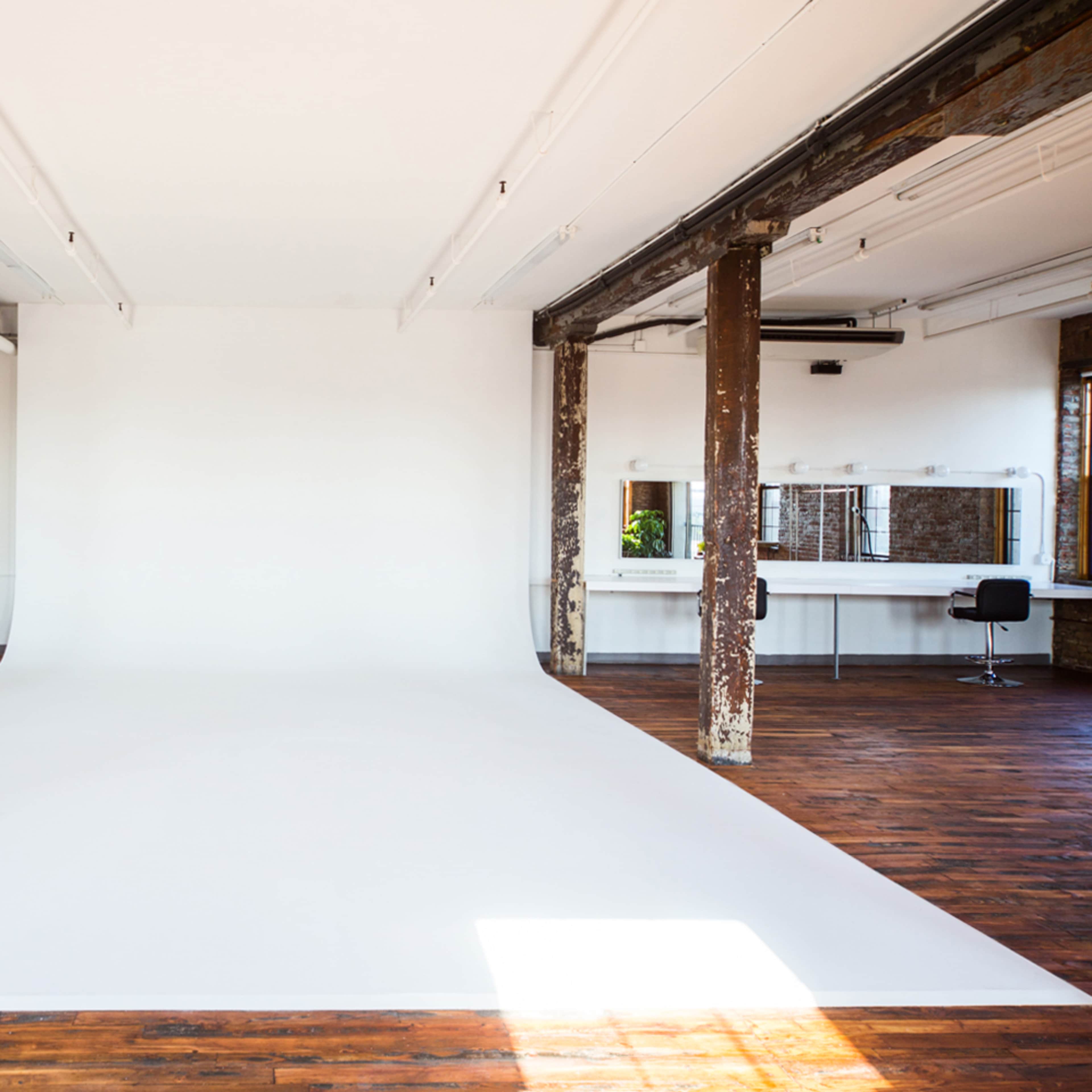 A spacious photography studio featuring a white backdrop, wooden floors, and exposed beams.