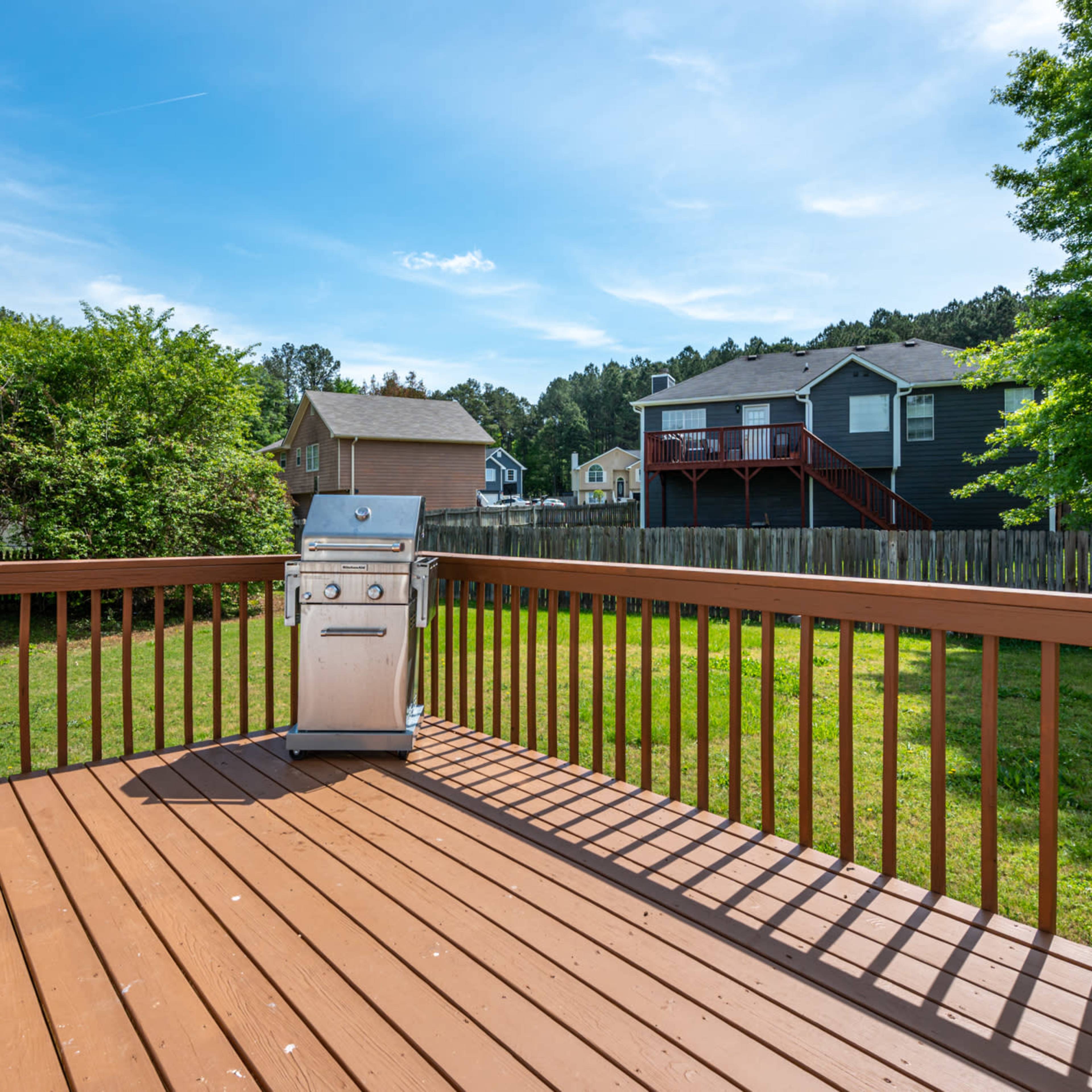 A stainless steel grill is positioned on a wooden deck overlooking a grassy backyard with houses in the background.