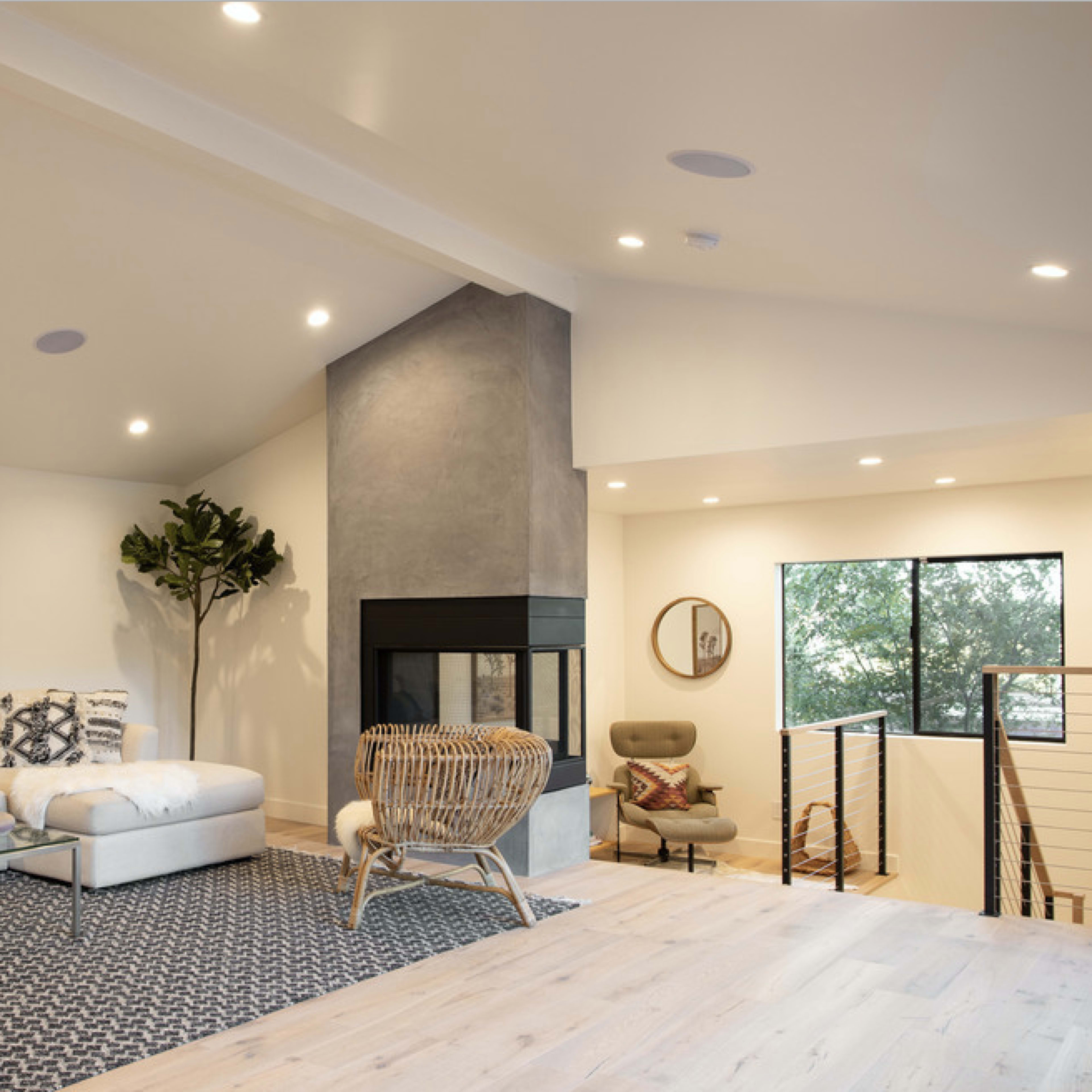 A modern living room features a sofa, a geometric rug, a fireplace, and large windows allowing natural light to enter the space.