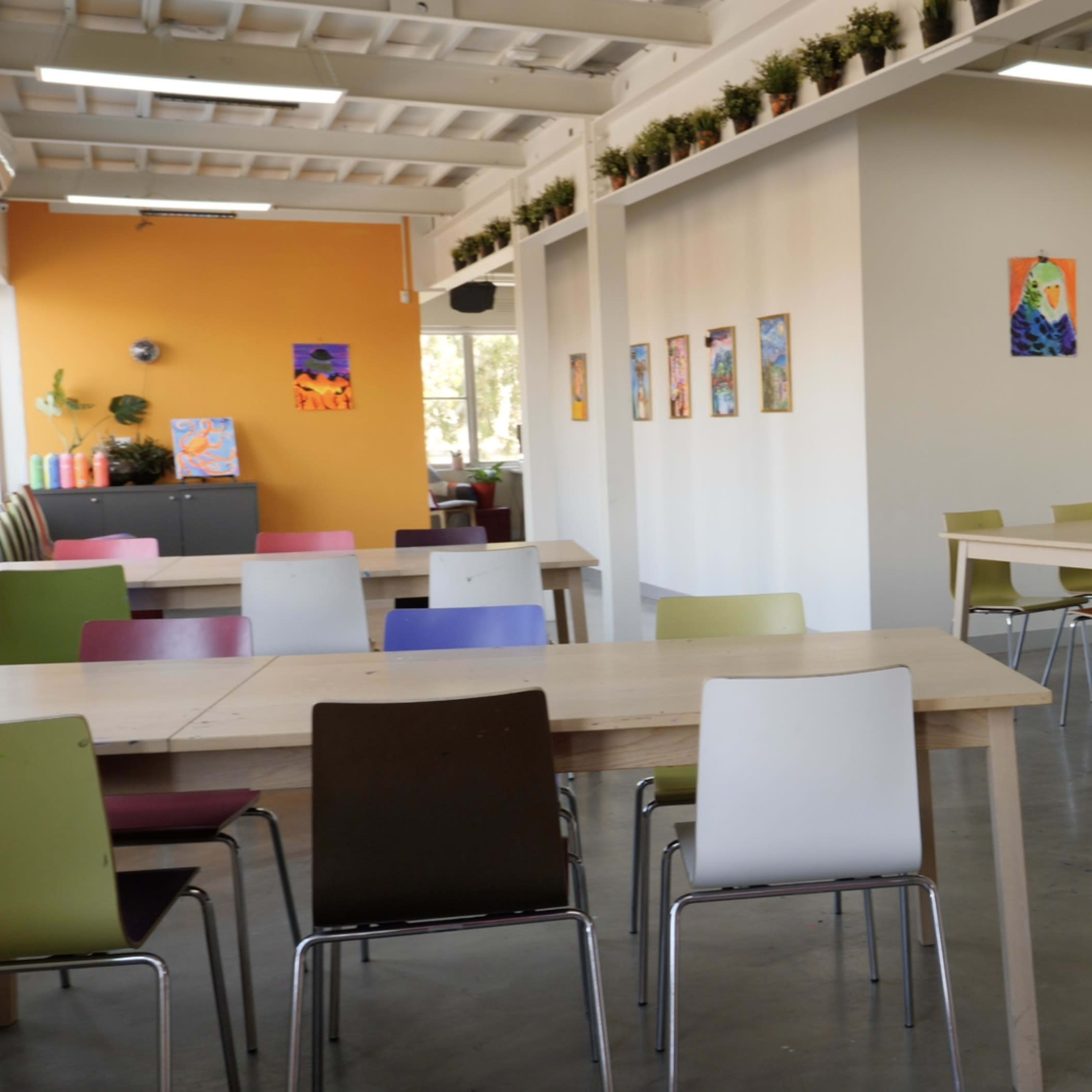 A modern dining area with several tables and chairs arranged around a bright room adorned with colorful artwork on the walls.