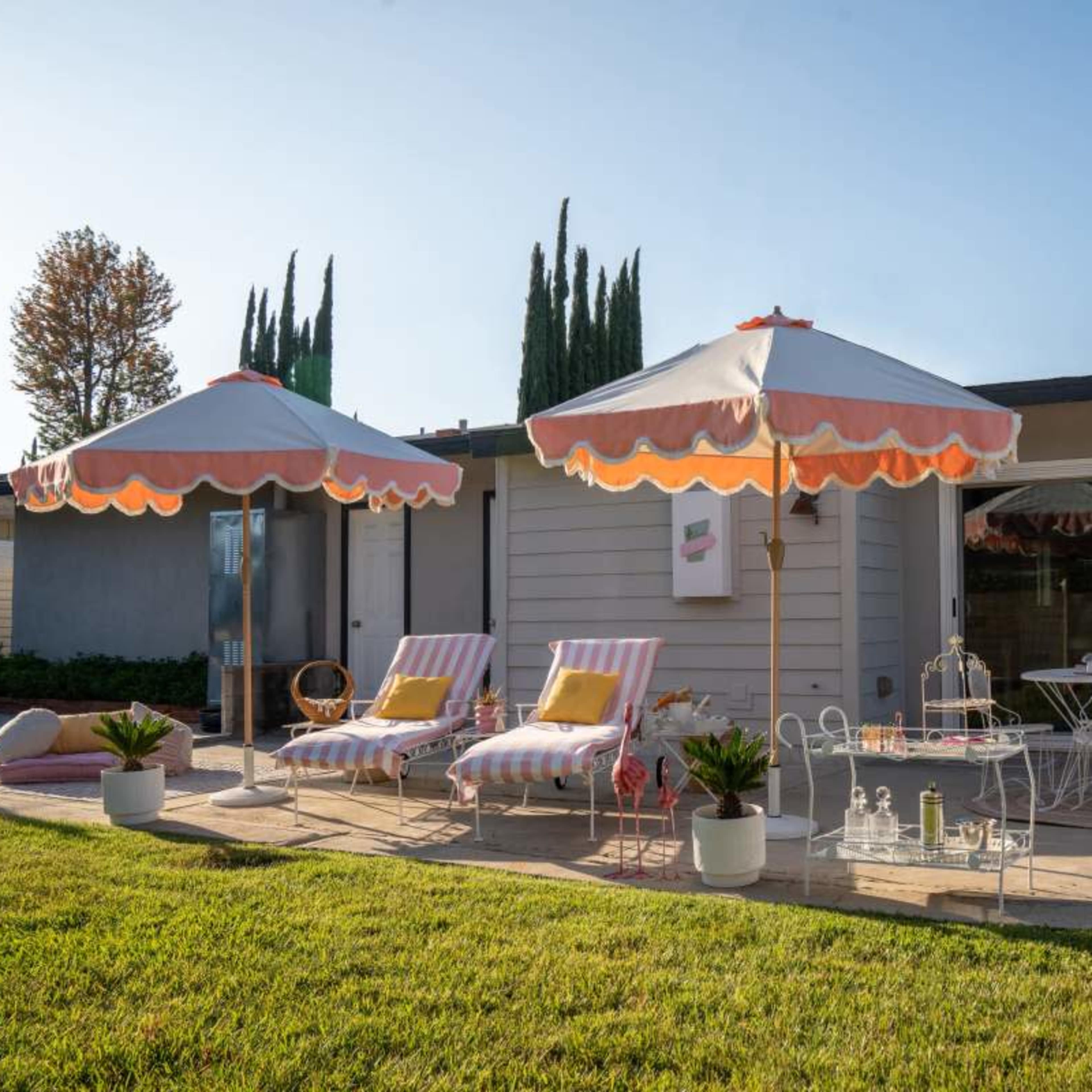 A patio area features striped lounge chairs, two large umbrellas, and a small table set against a house with a large glass door.