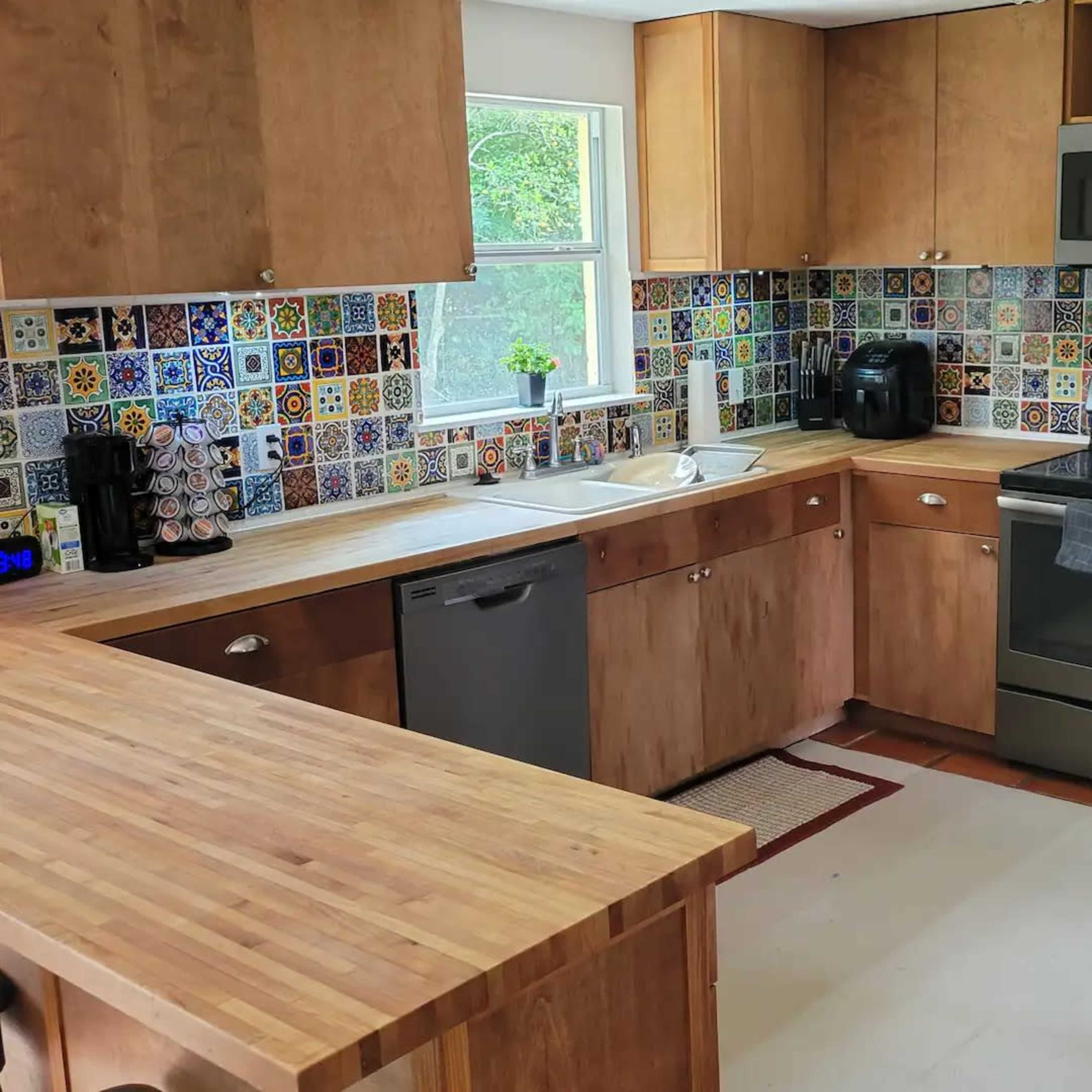 A kitchen with wooden cabinets, colorful tiled backsplash, stainless steel appliances, and a central wooden island.
