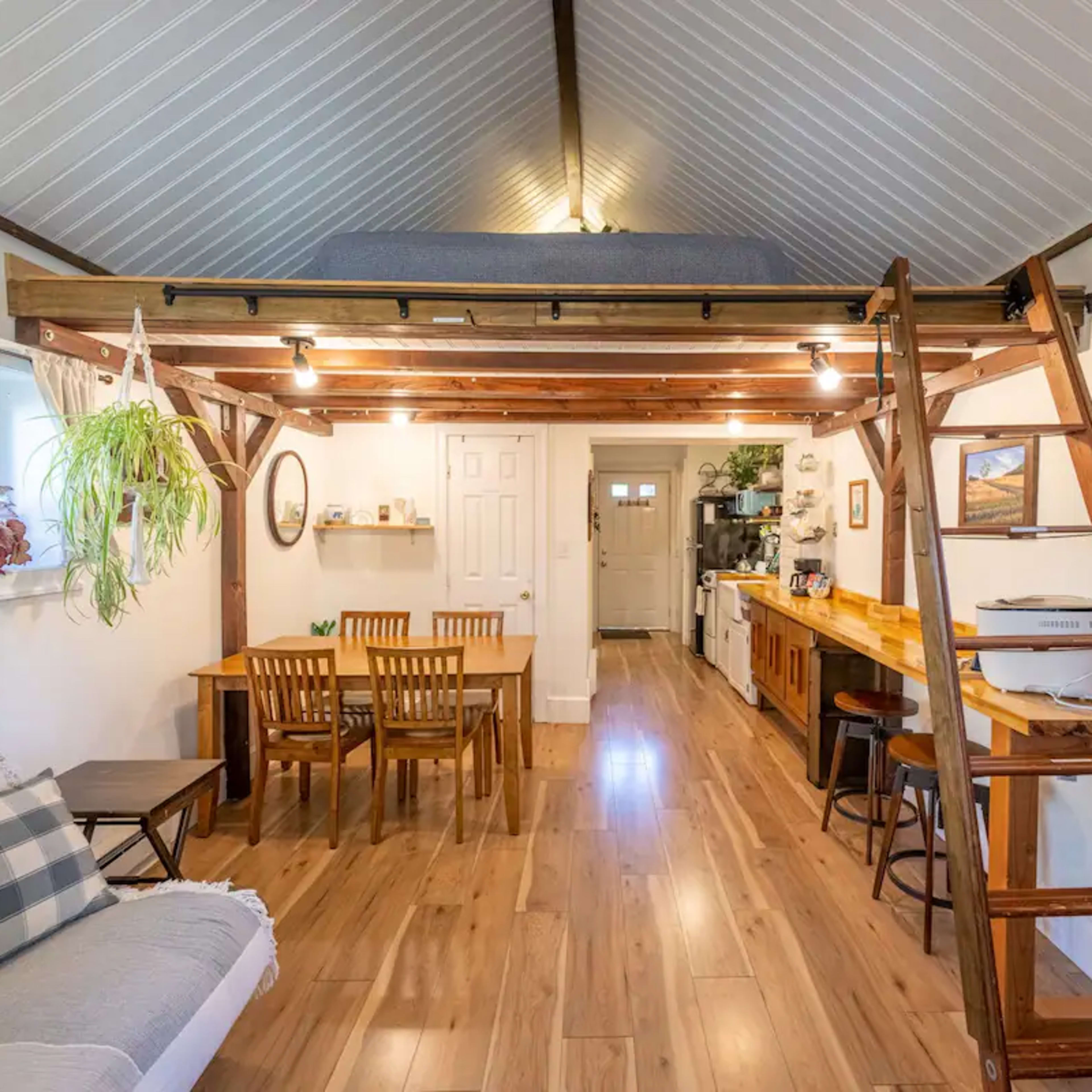 A small, open-concept living area featuring a wooden loft, a dining table, and a kitchen along one wall.