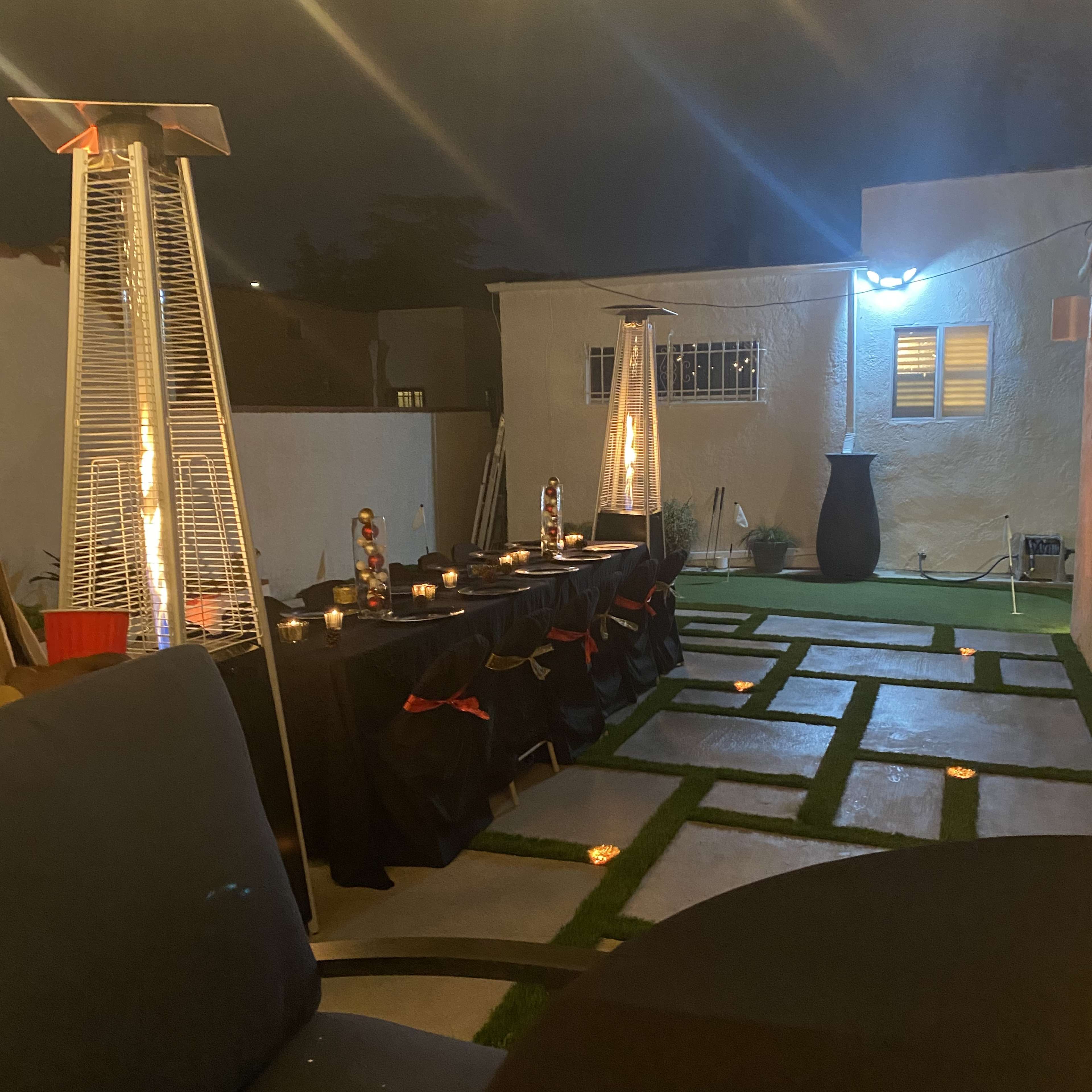 A patio area is set up for an evening event, featuring several tables with black tablecloths and decorative lighting.