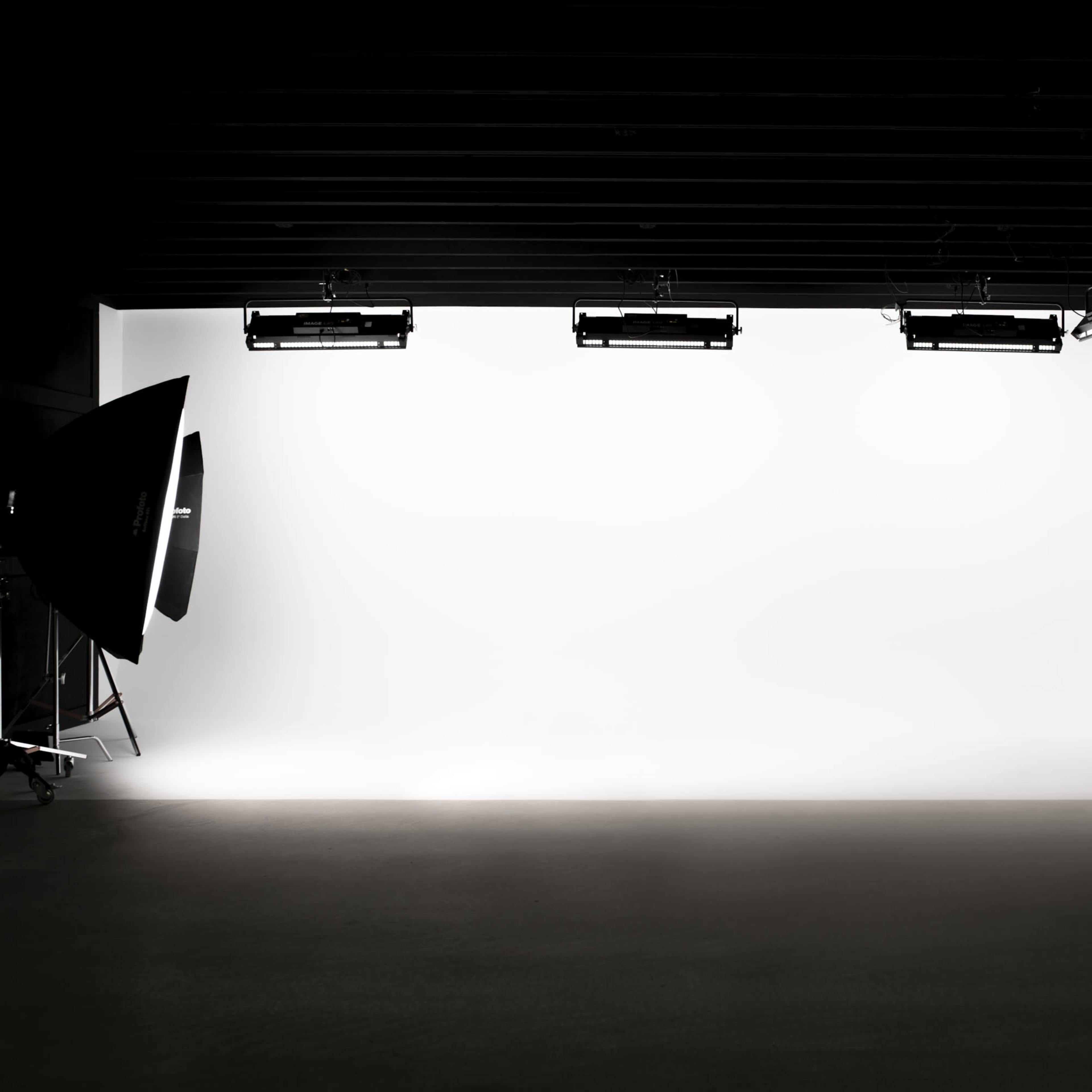 A photography studio with a large white backdrop and three overhead lights.