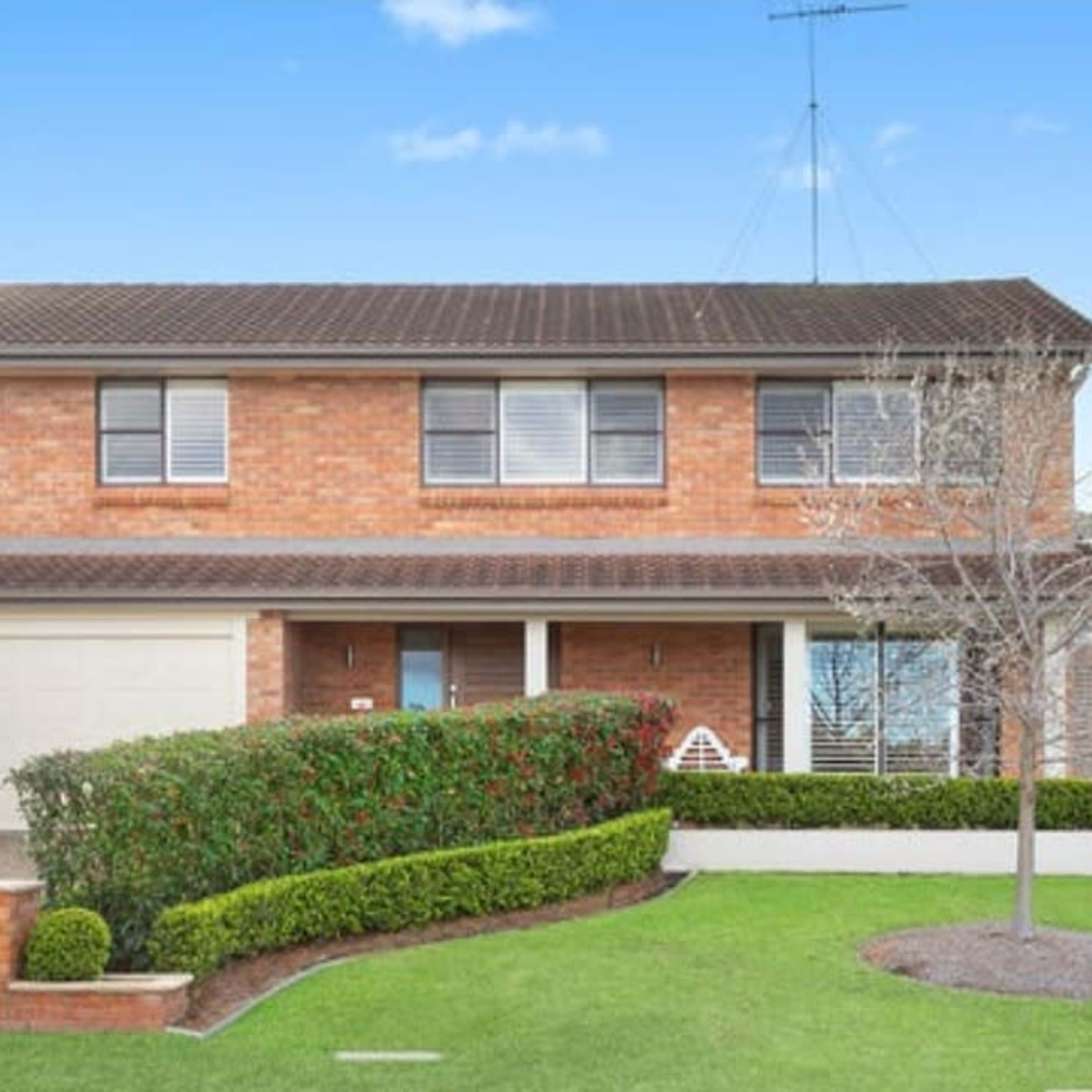 A two-story brick house with a neatly landscaped front yard and a paved driveway.