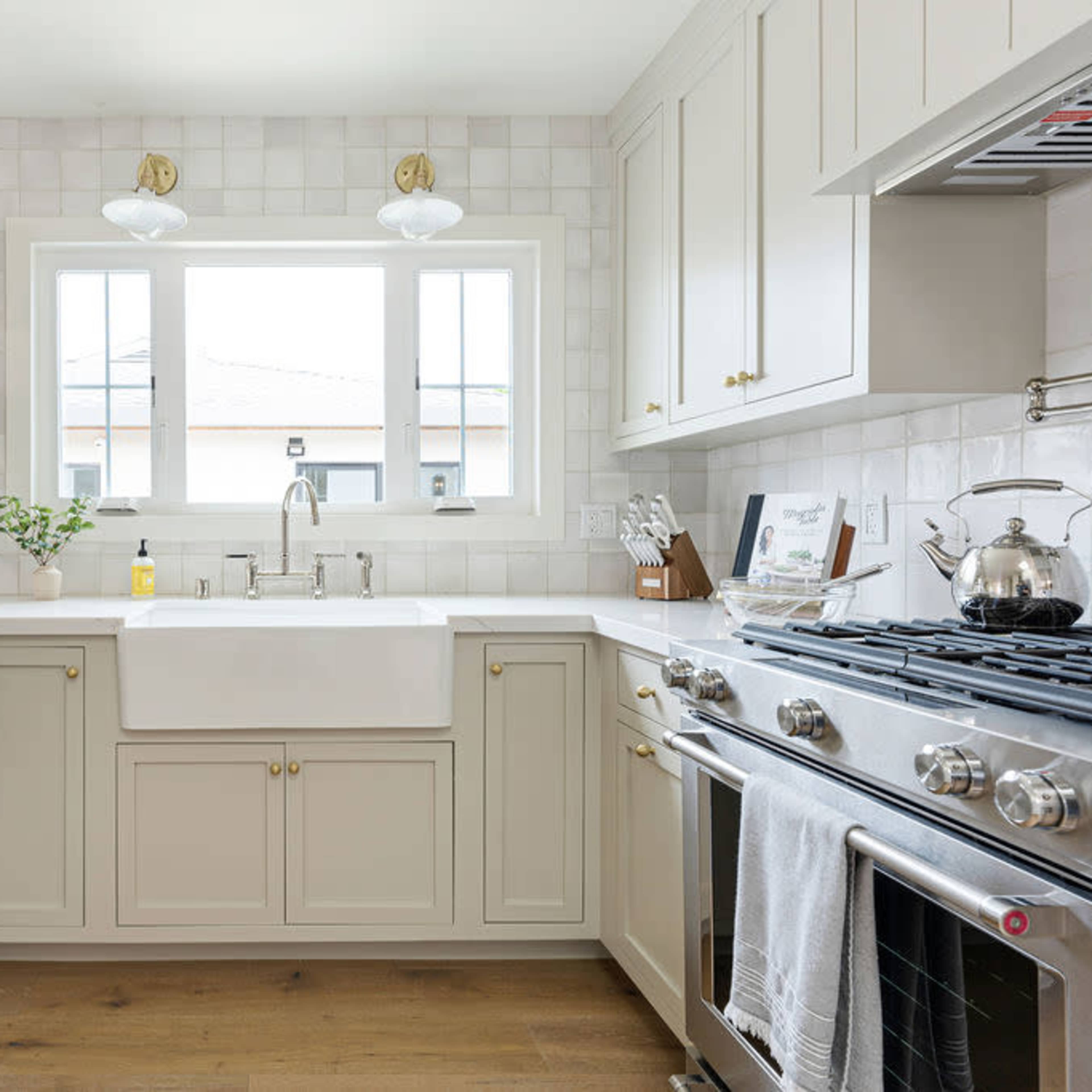 A modern kitchen features a farmhouse sink, stainless steel appliances, and light-colored cabinetry against a tiled backsplash.