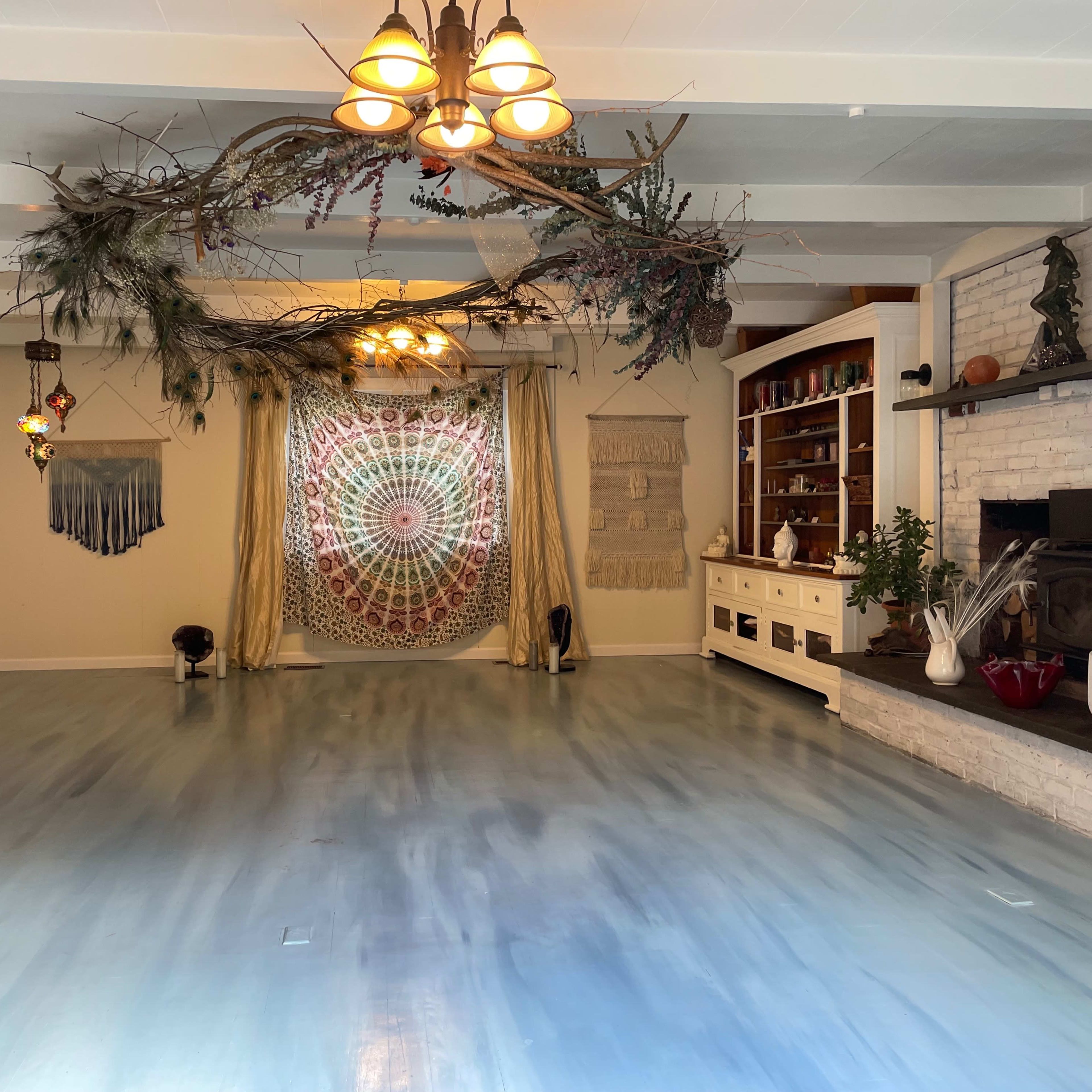 The spacious room features a patterned wall hanging, a rustic white-brick fireplace, and decorative elements suspended from the ceiling.