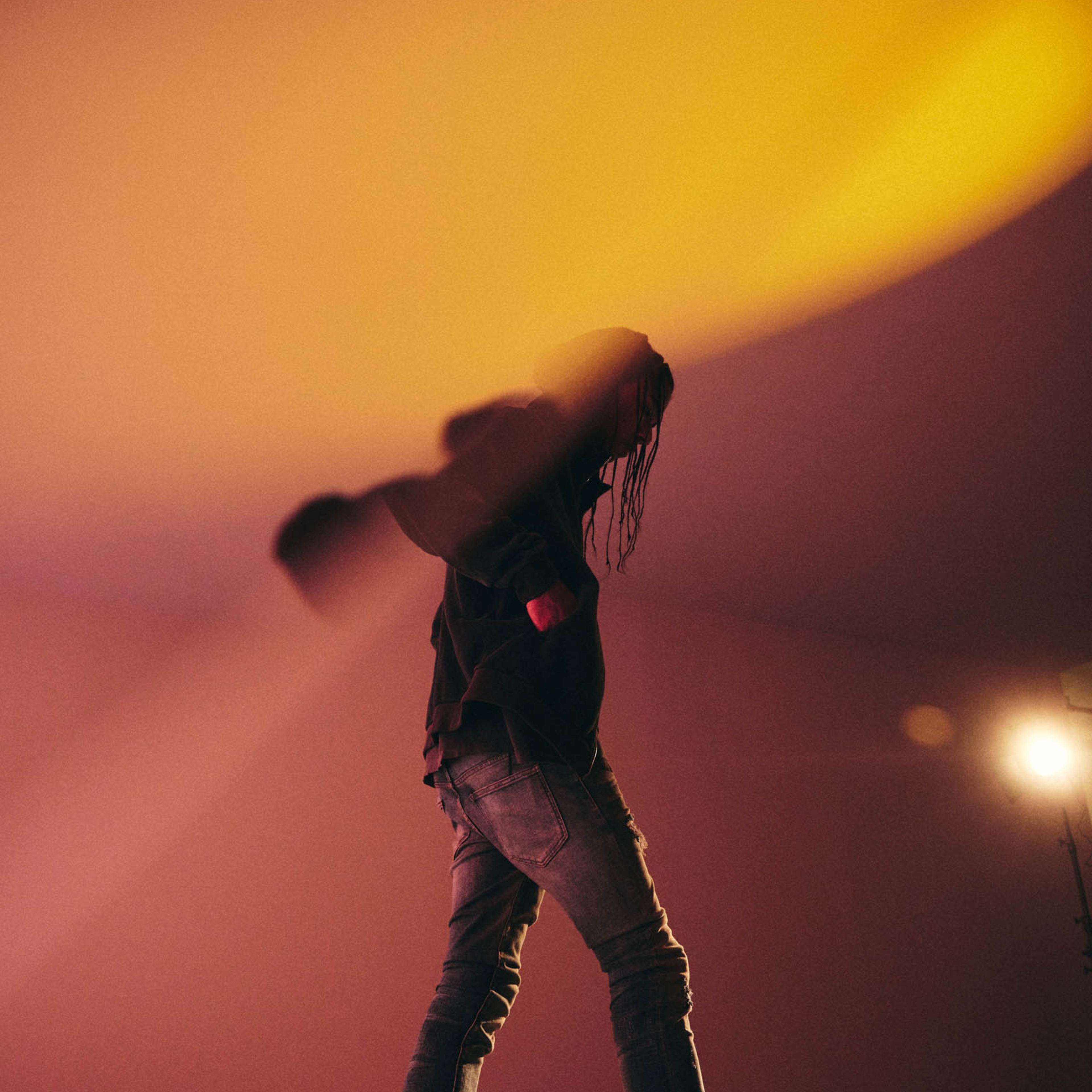 A person wearing a dark shirt and jeans walks under a warm light in an indoor setting.