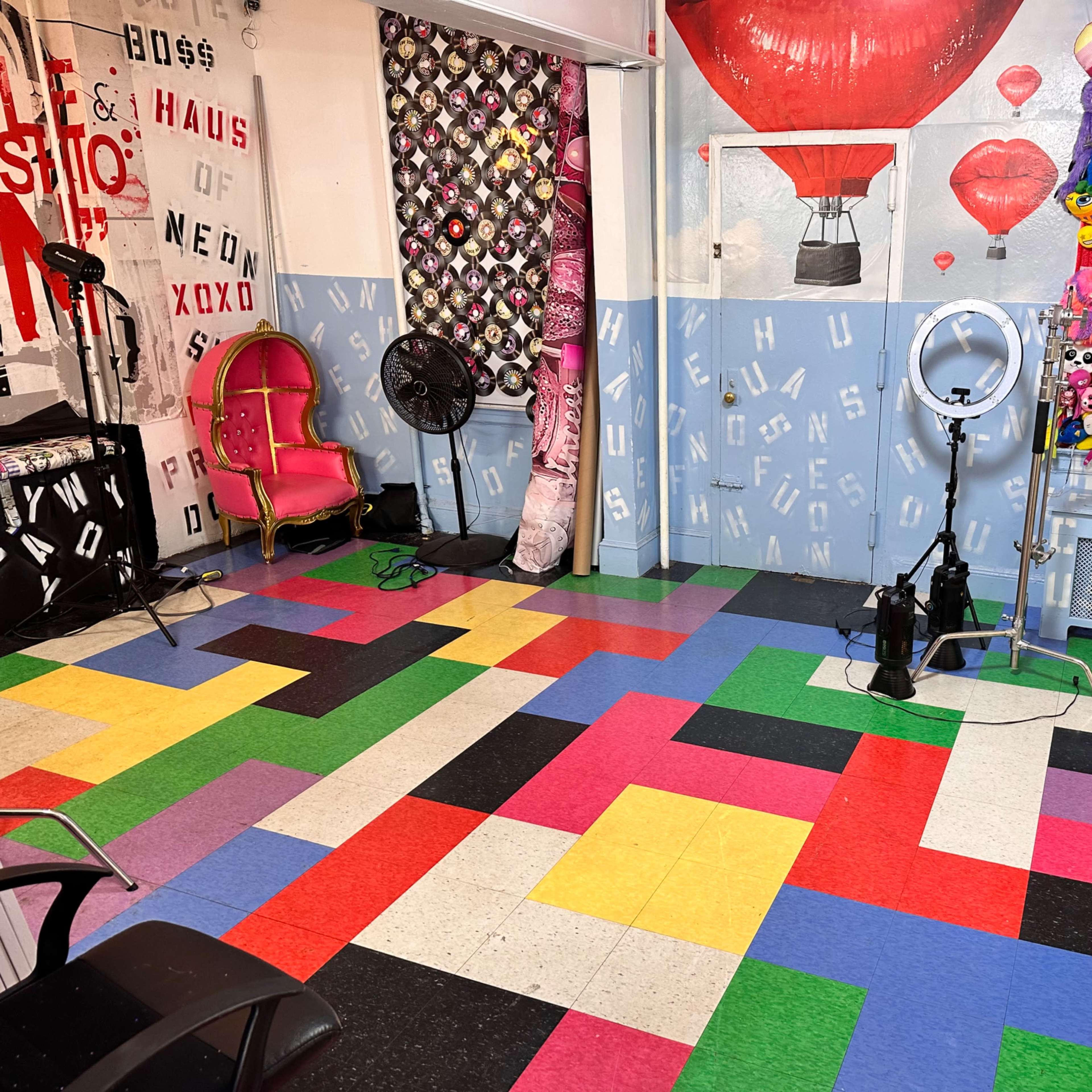 A colorful floor made of interlocking tiles in a studio setting, featuring a pink chair and a wall adorned with plush toys and various decorative elements.