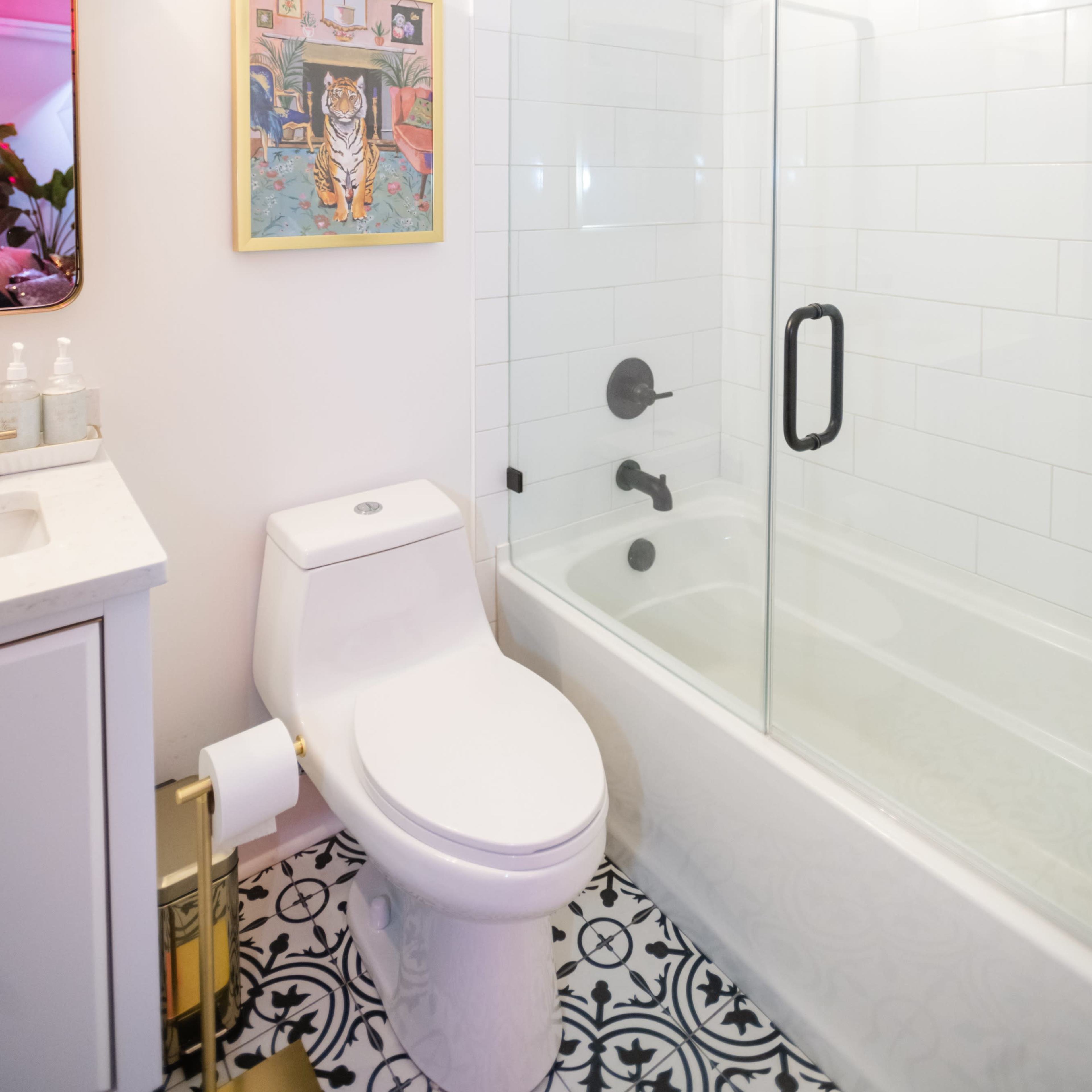 A modern bathroom featuring a shower-tub combo with glass doors, a wall-mounted faucet, a toilet, and decorative tile flooring.