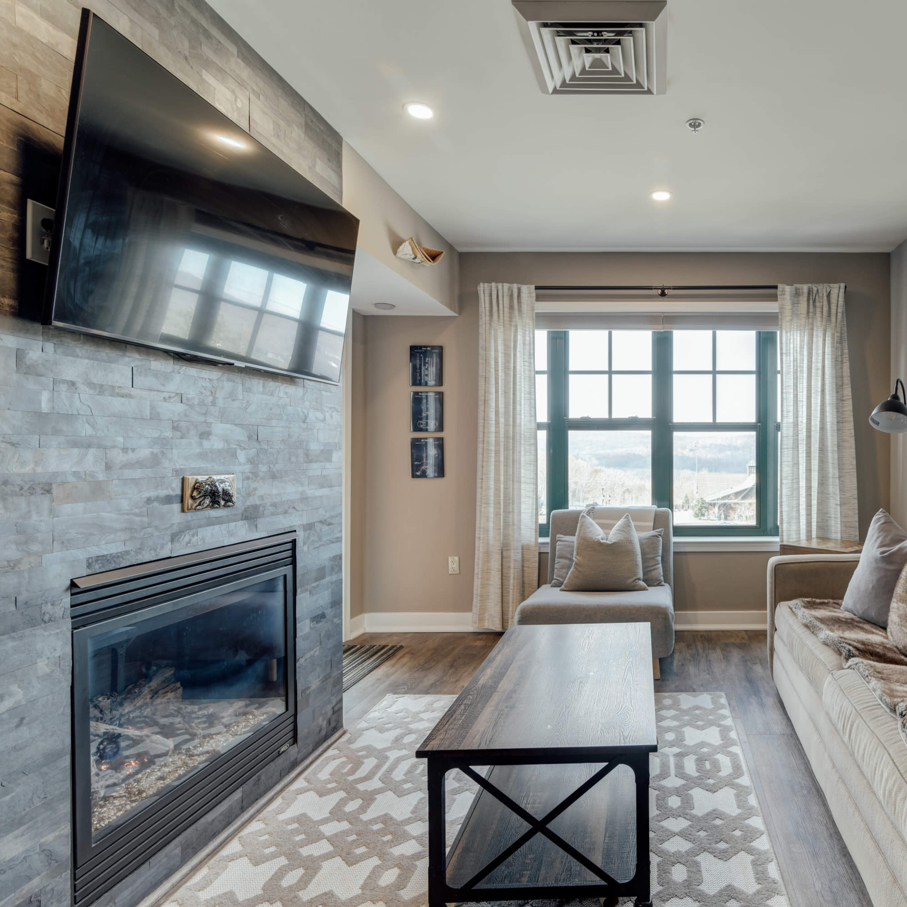 A living room with a fireplace, a sofa, a coffee table, and a large window overlooking a mountain view.