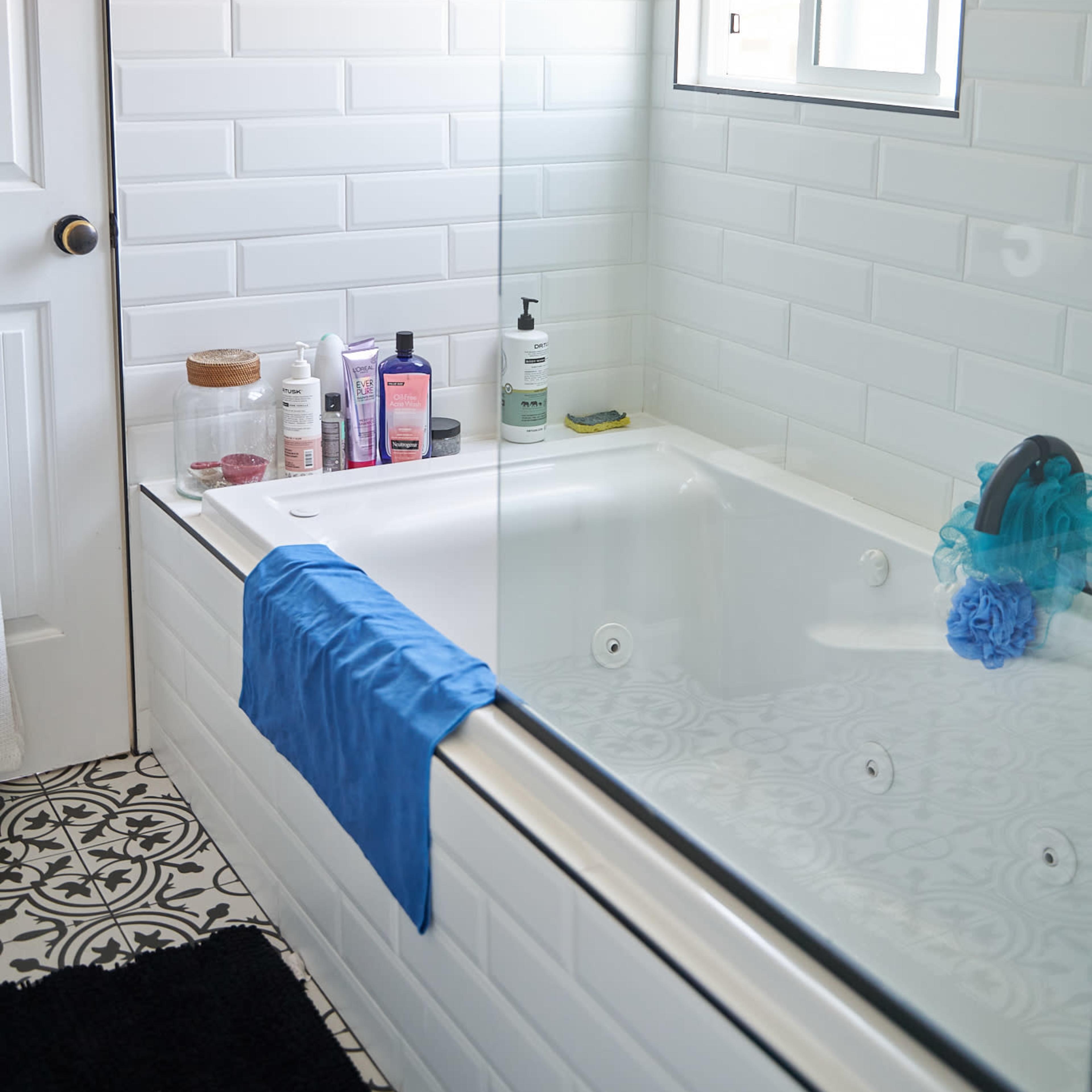 A clean bathroom with a bathtub, a shower partition, various toiletries on the edge, and a window allowing natural light.