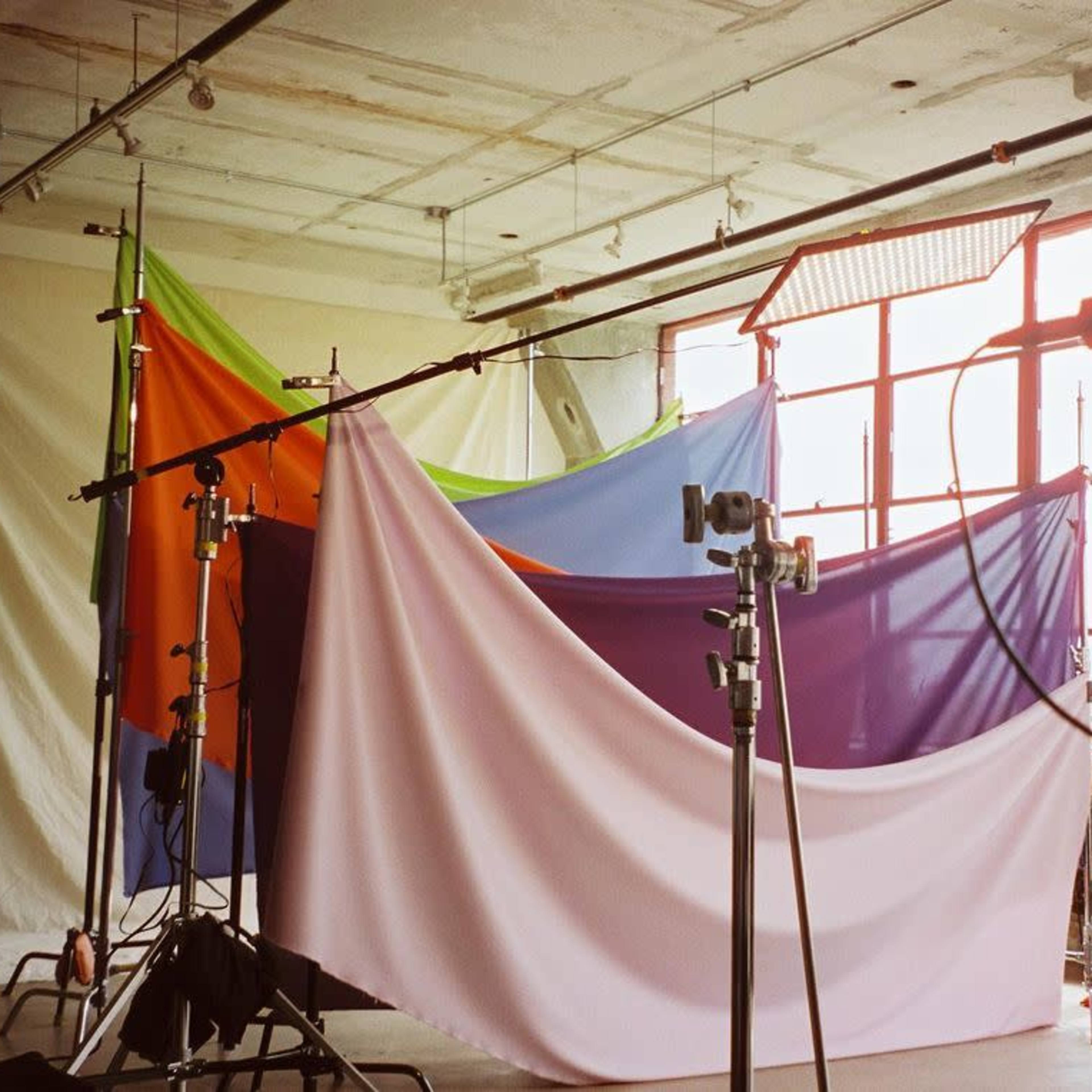 A photography studio with colorful backdrops draped over stands and large windows allowing natural light to enter the space.