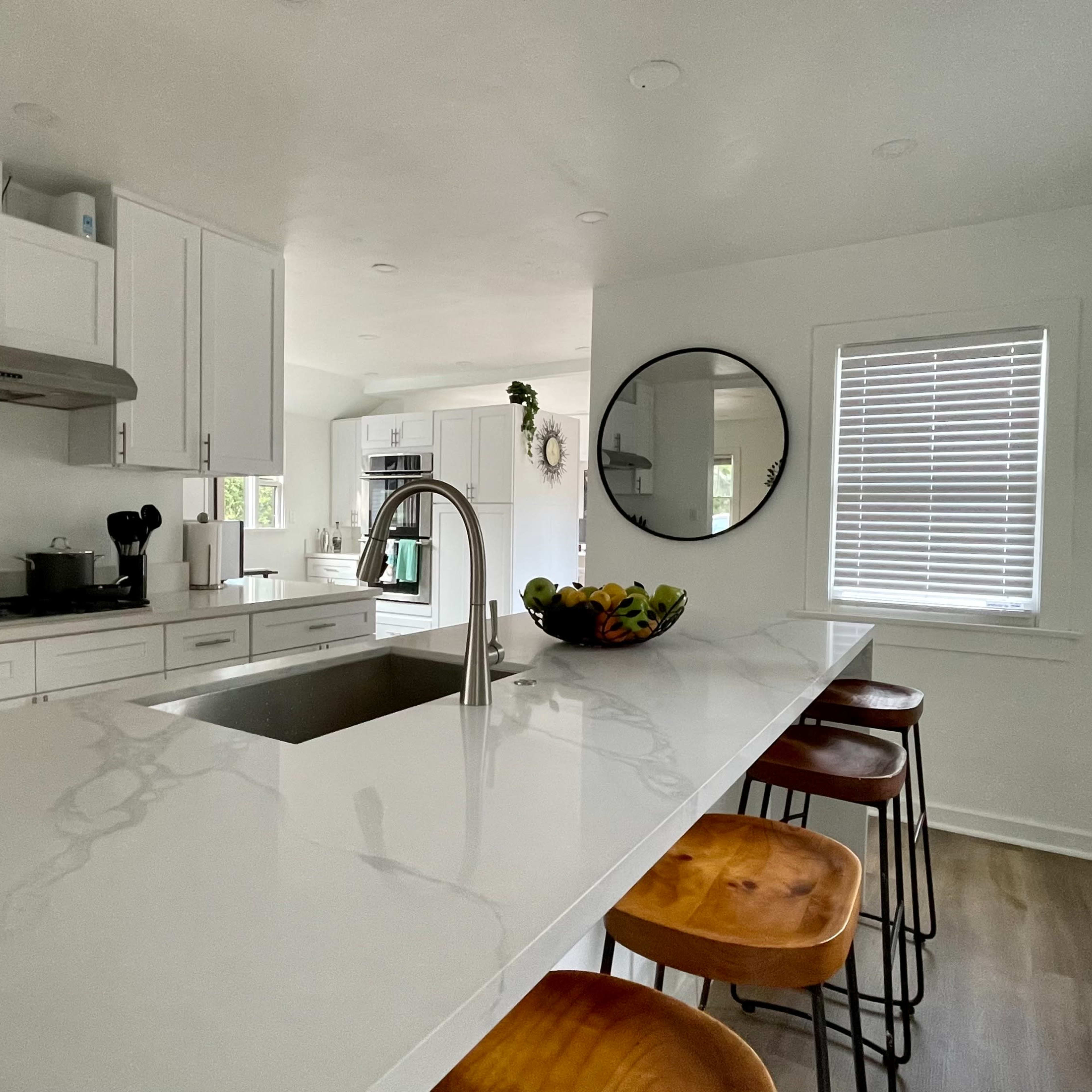 A modern kitchen features white cabinetry, a large island with a sink, and three wooden bar stools.