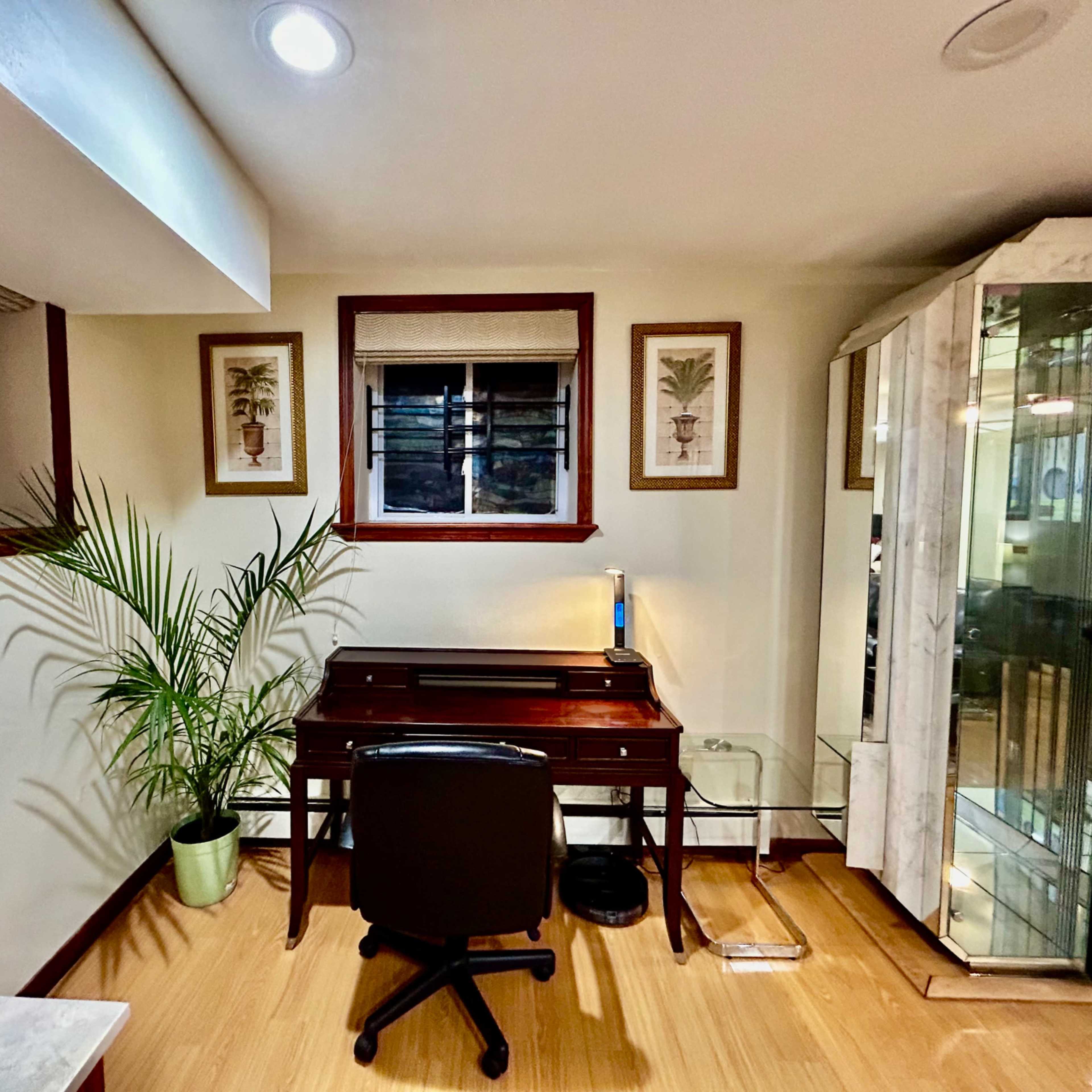 A small office space with a wooden desk, a chair, and framed botanical prints on the walls, alongside a potted plant in the corner.