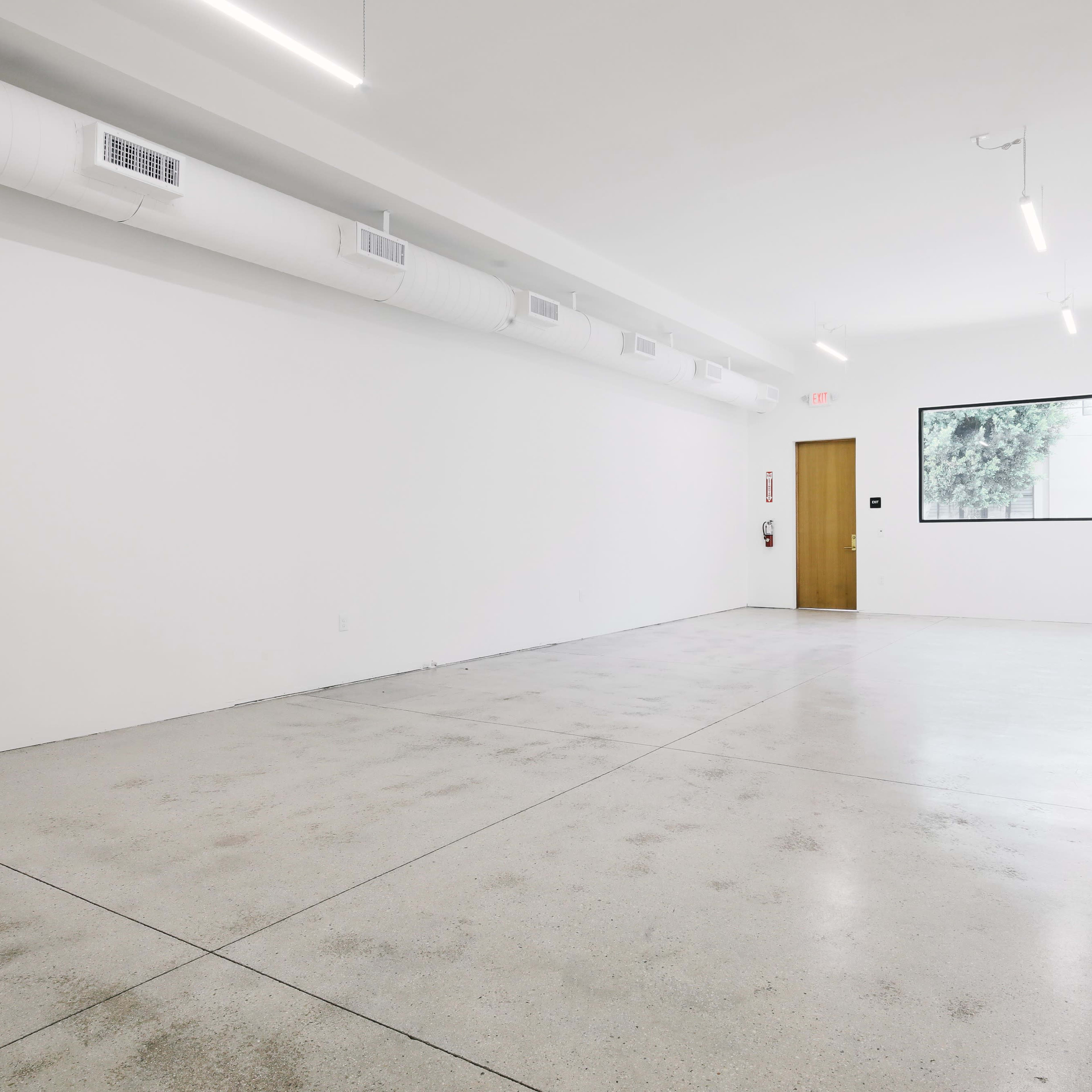 An empty room with a polished concrete floor, white walls, and a window on the far side.